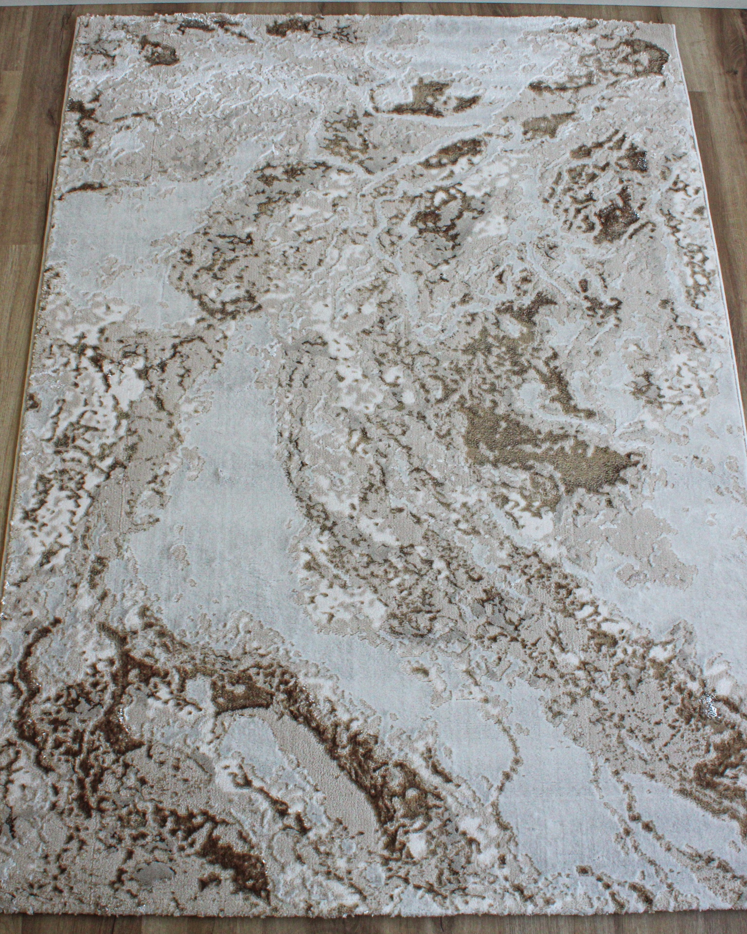 Tapete retangular bege e castanho com padrão abstrato sobre chão de madeira