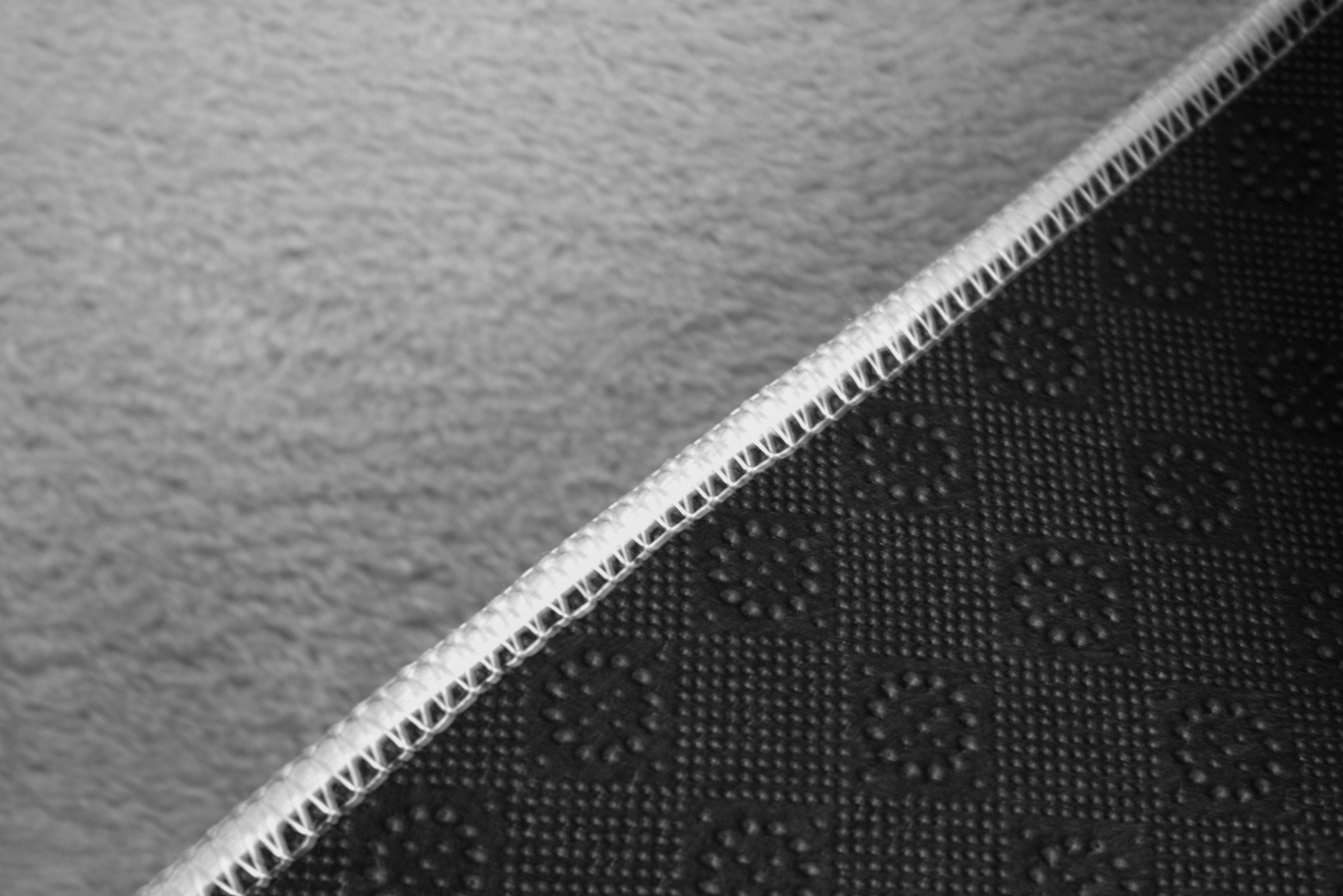 Tapete texturizado preto com padrão circular e margem costurada sobre chão rugoso