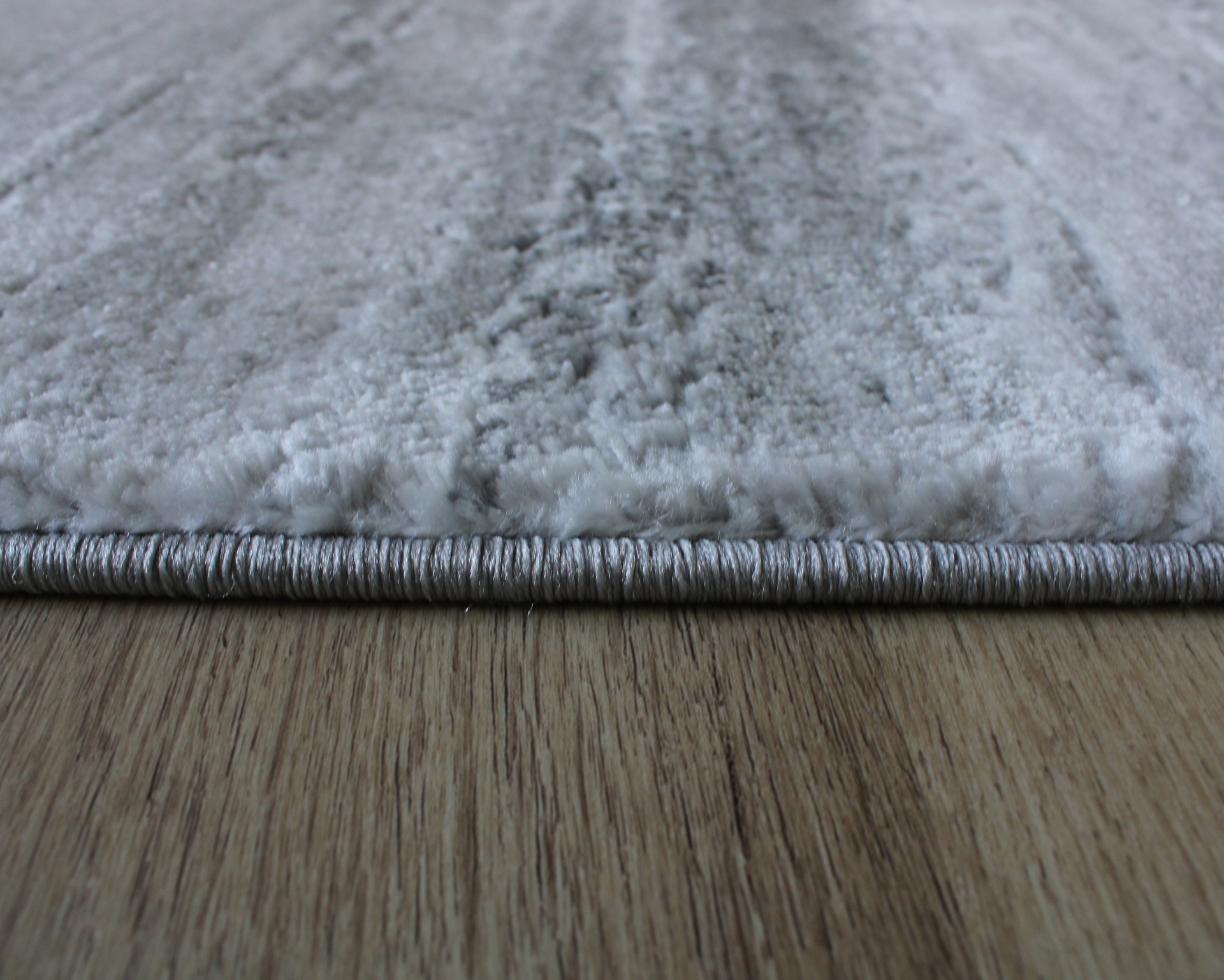 Tapete cinza claro com textura felpuda e borda cinza escura sobre chão de madeira clara