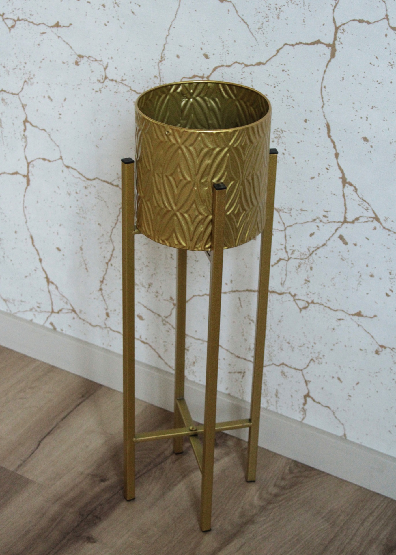 Suporte de vaso dourado com padrão geométrico em relevo junto a parede
