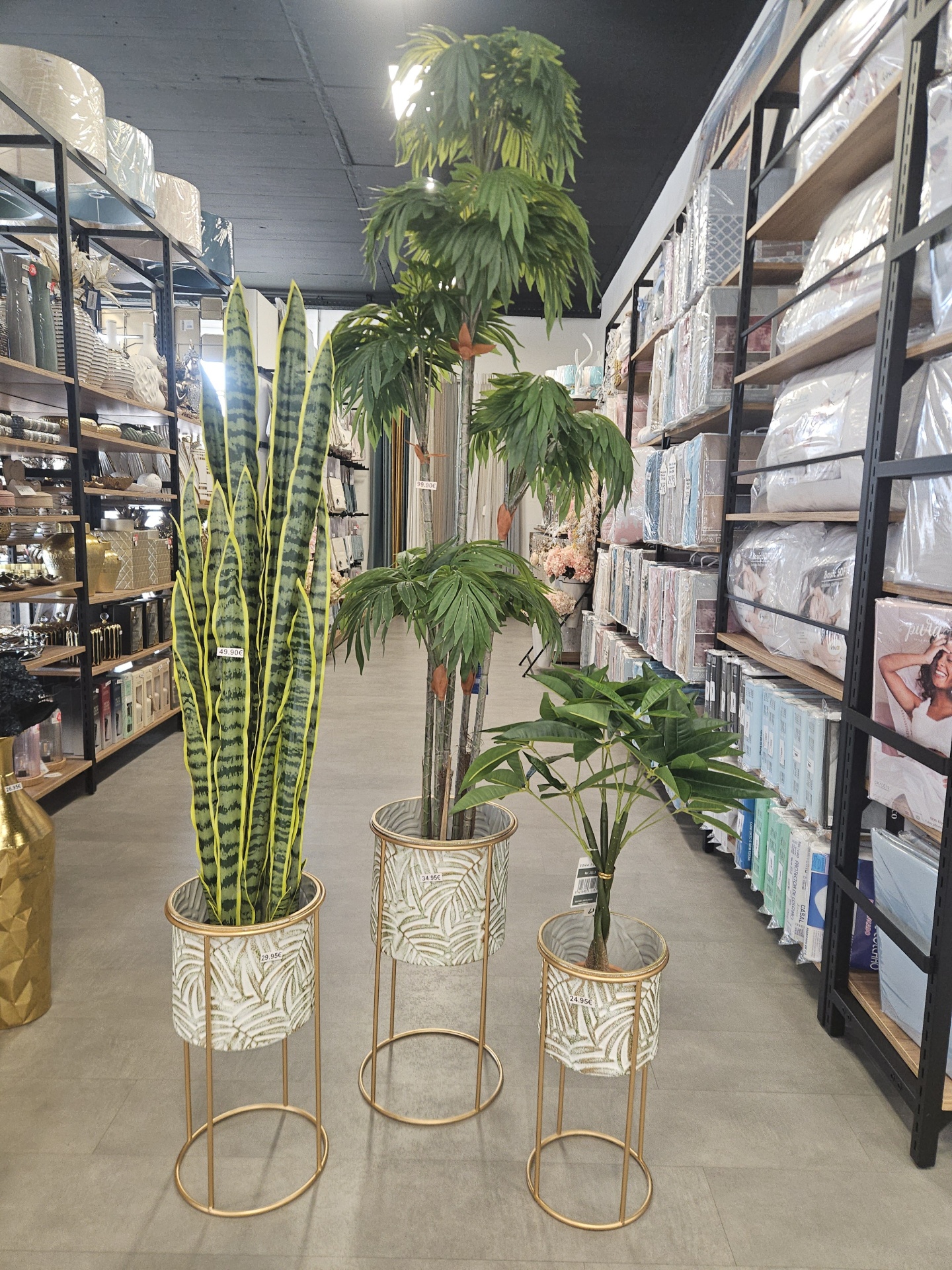 Três vasos com plantas artificiais verdes em ambiente de loja com prateleiras