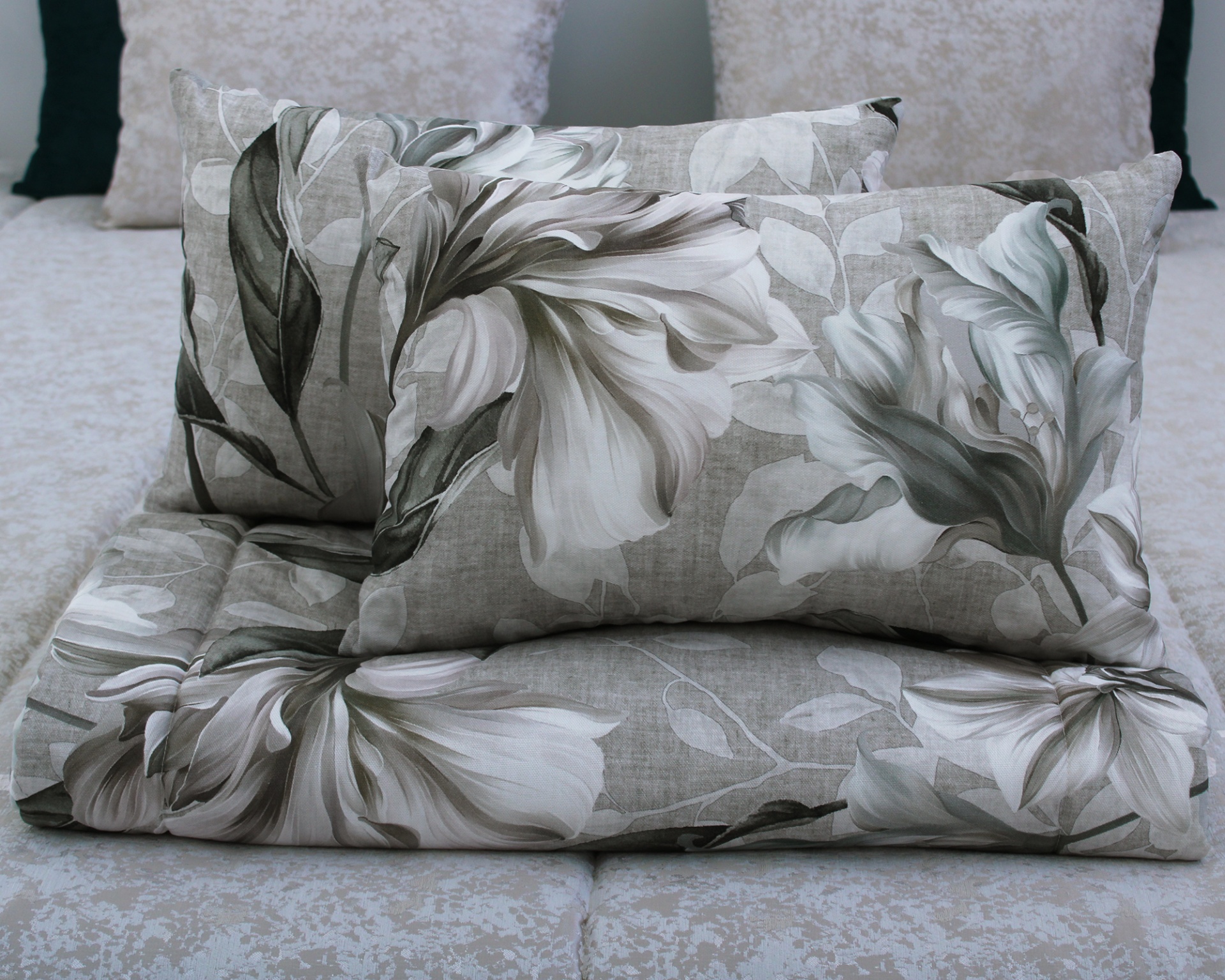 Almofadas e edredão florais cinza e branco sobre cama.