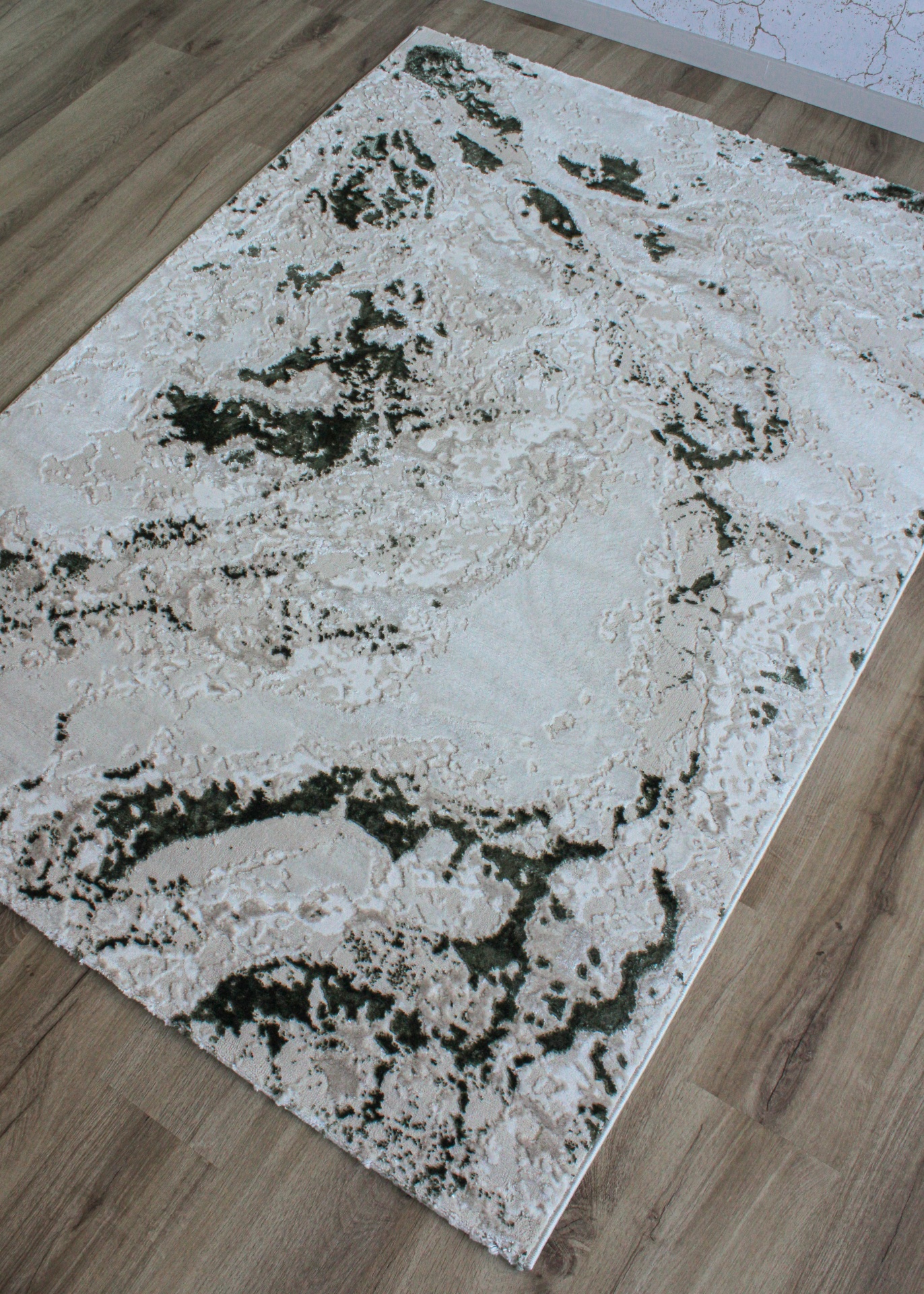 Tapete retangular abstrato creme, bege e verde-escuro em chão de madeira