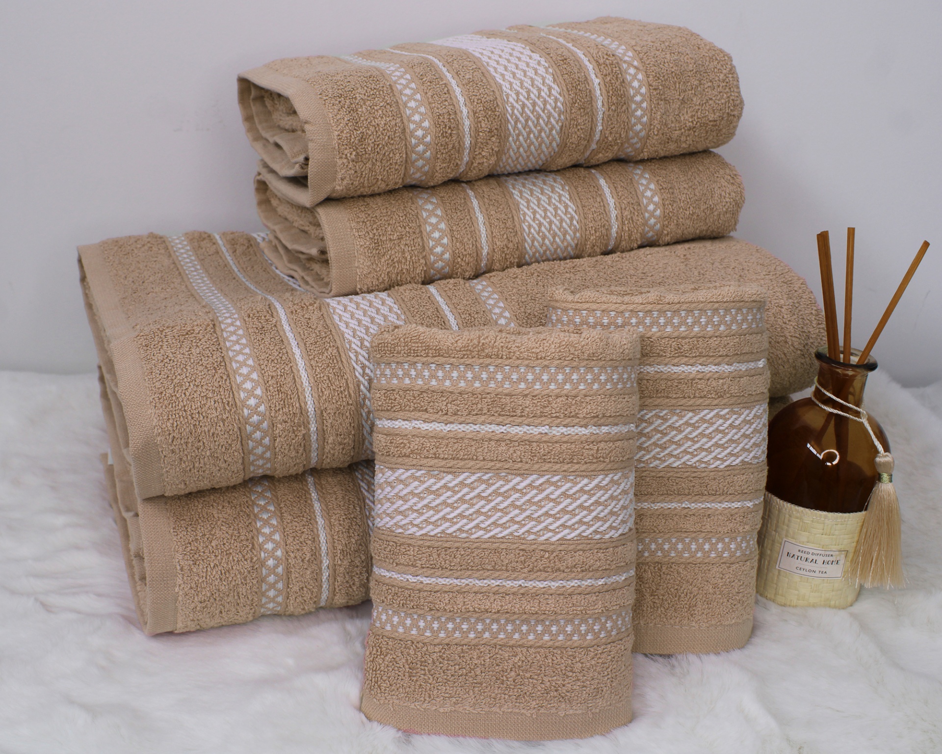 Conjunto de toalhas bege com riscas brancas e difusor de aroma castanho com pauzinhos