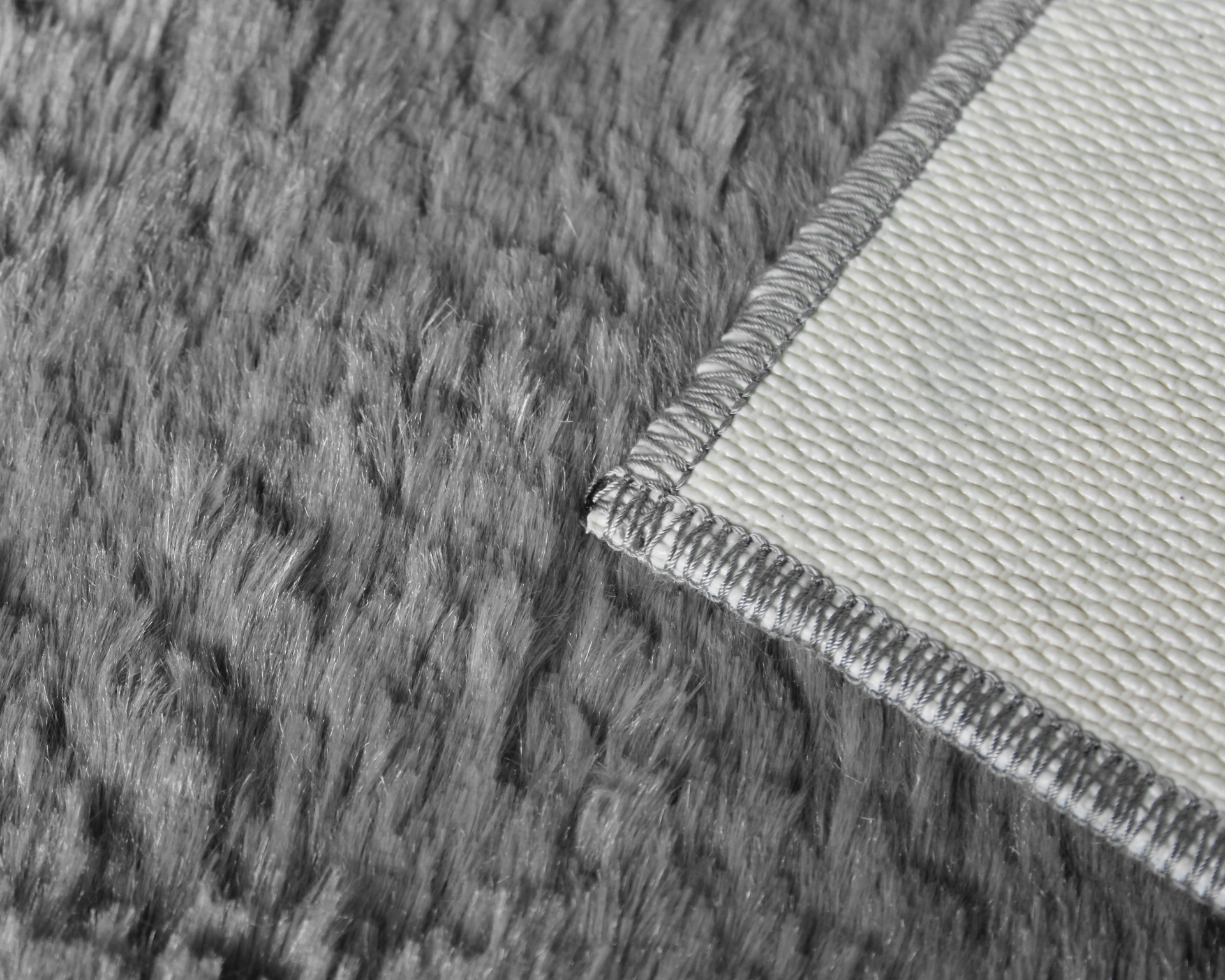 Tapete cinzento macio com canto de tecido branco e costura cinzenta