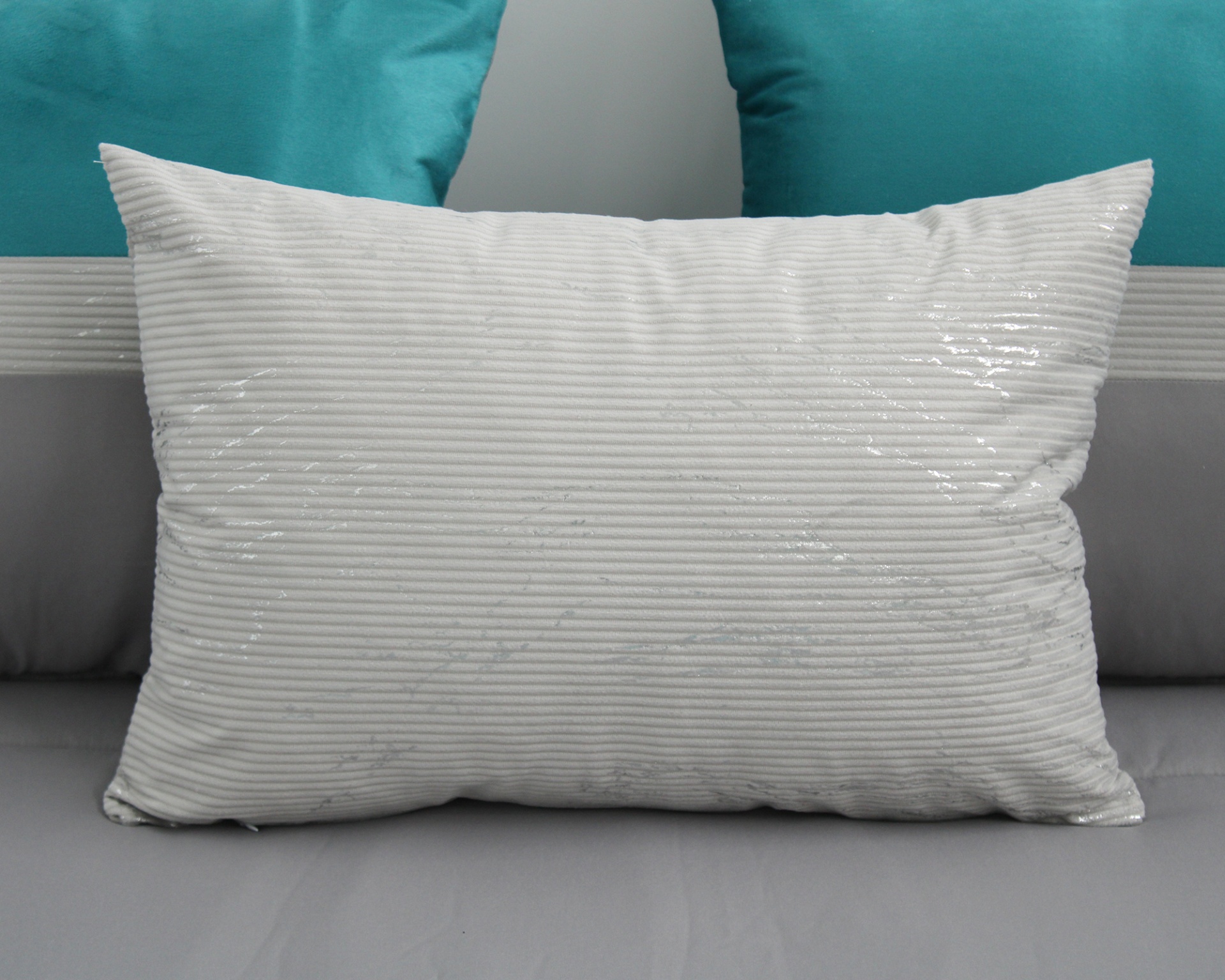 Travesseiro branco com riscas finas e detalhes brilhantes numa cama com almofadas azuis e cinzentas