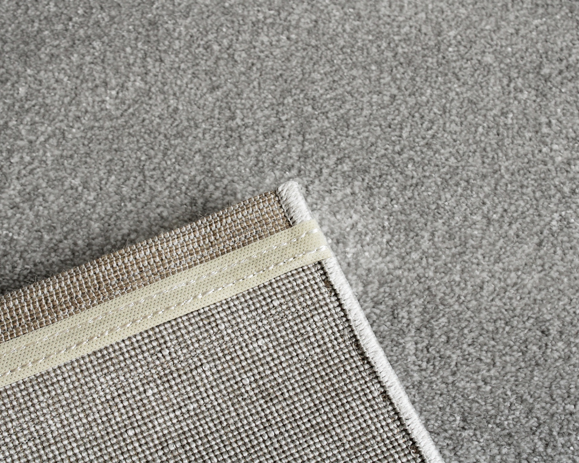 Tapete cinzento de tecido com bordas bege e costuras brancas sobre chão cinzento