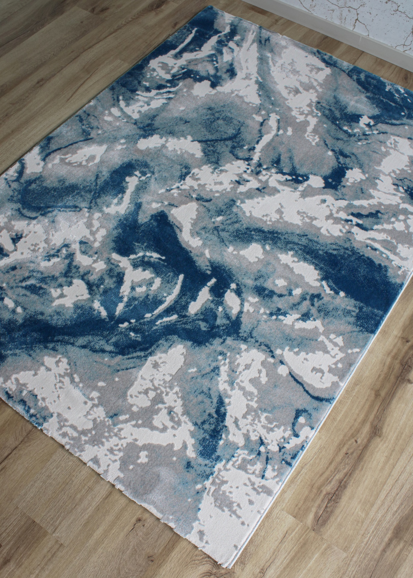 Tapete decorativo abstrato azul, cinzento e branco no chão de madeira