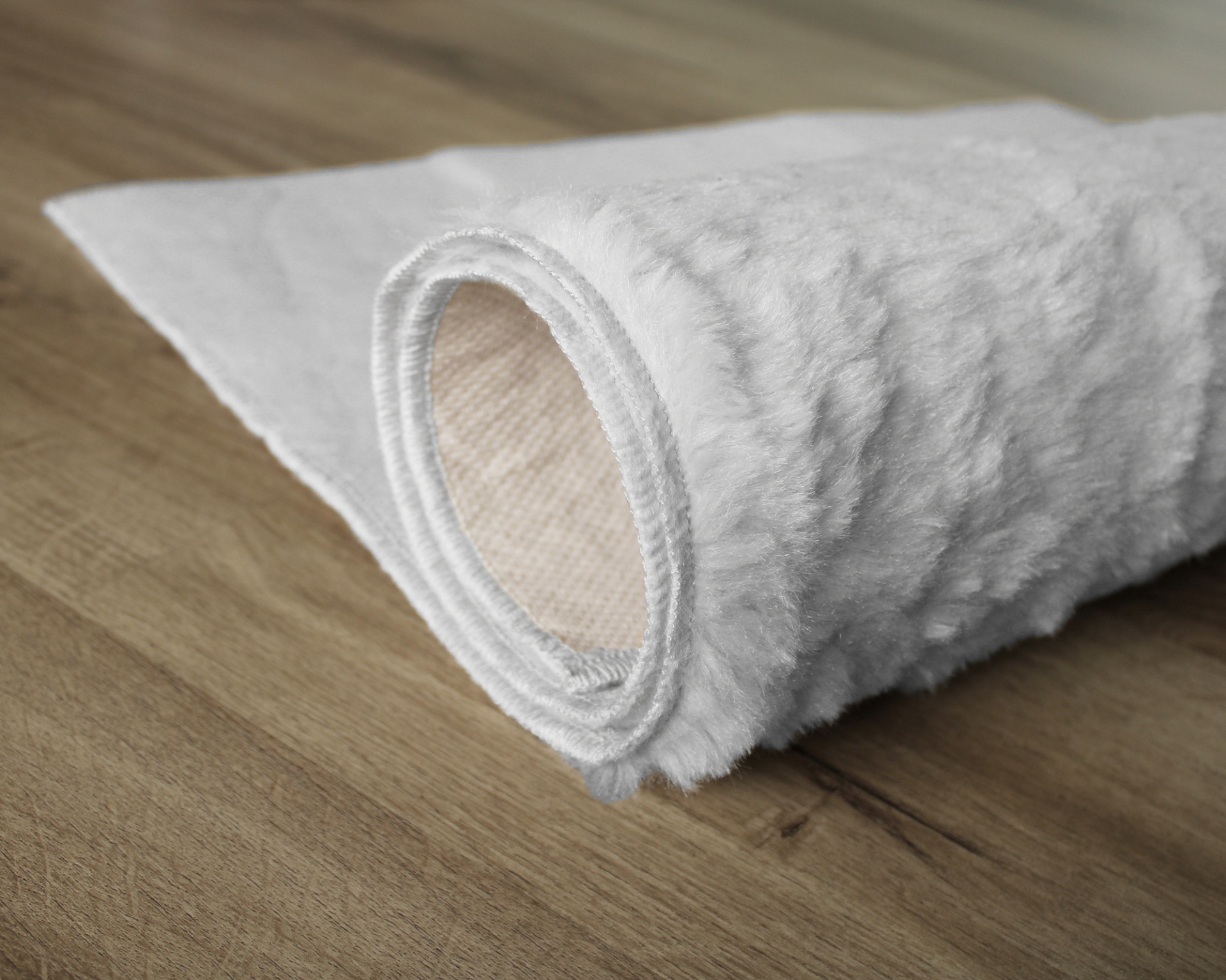 Tapete branco felpudo enrolado sobre piso de madeira clara