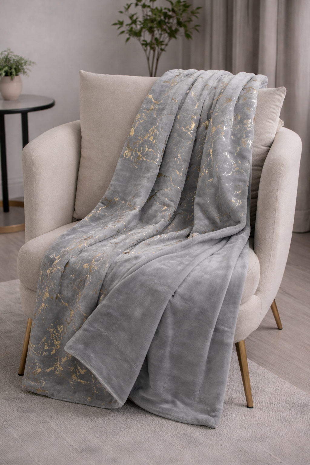 Manta cinza com padrão dourado sobre poltrona bege com pés dourados em sala