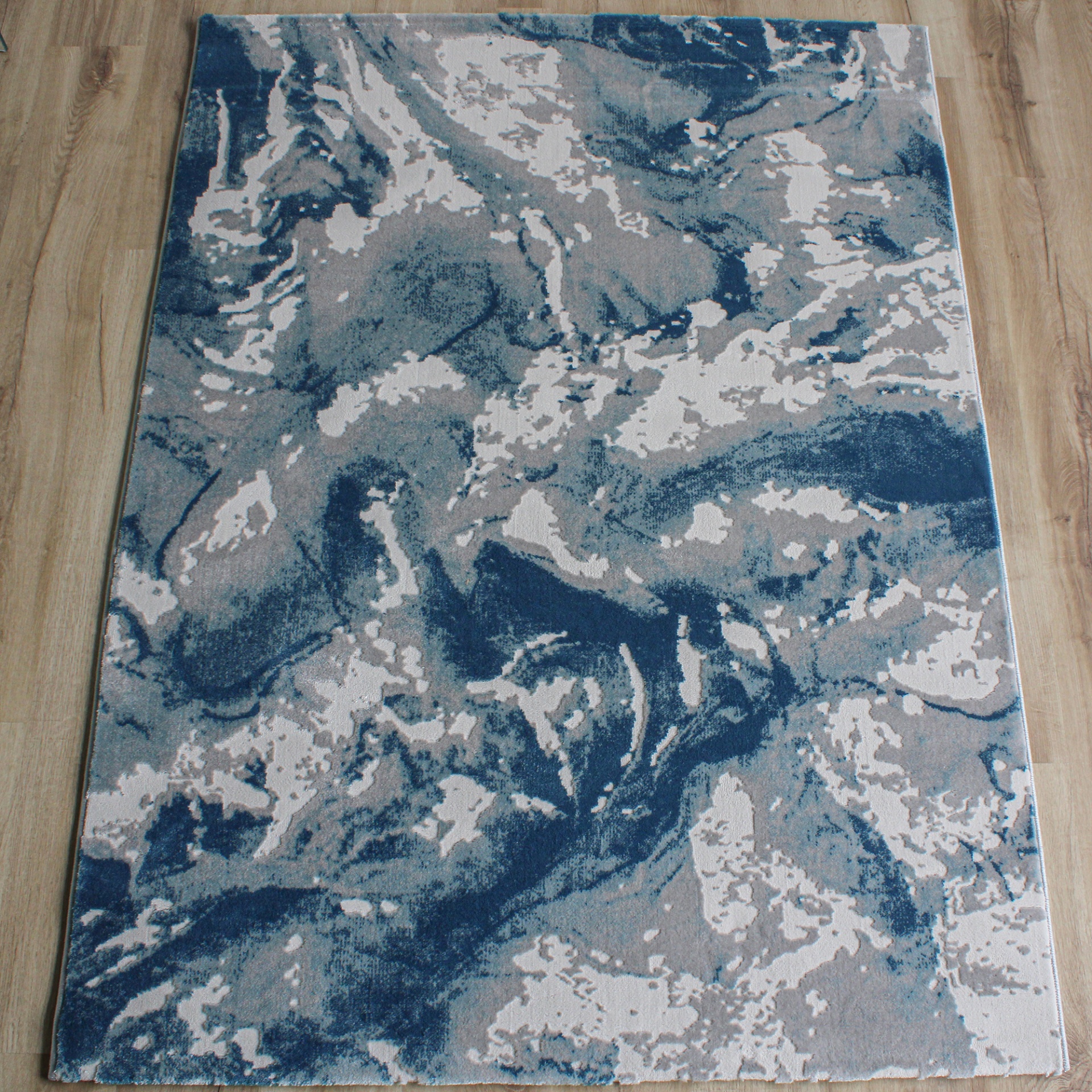 Tapete abstrato azul, cinza e branco em chão de madeira