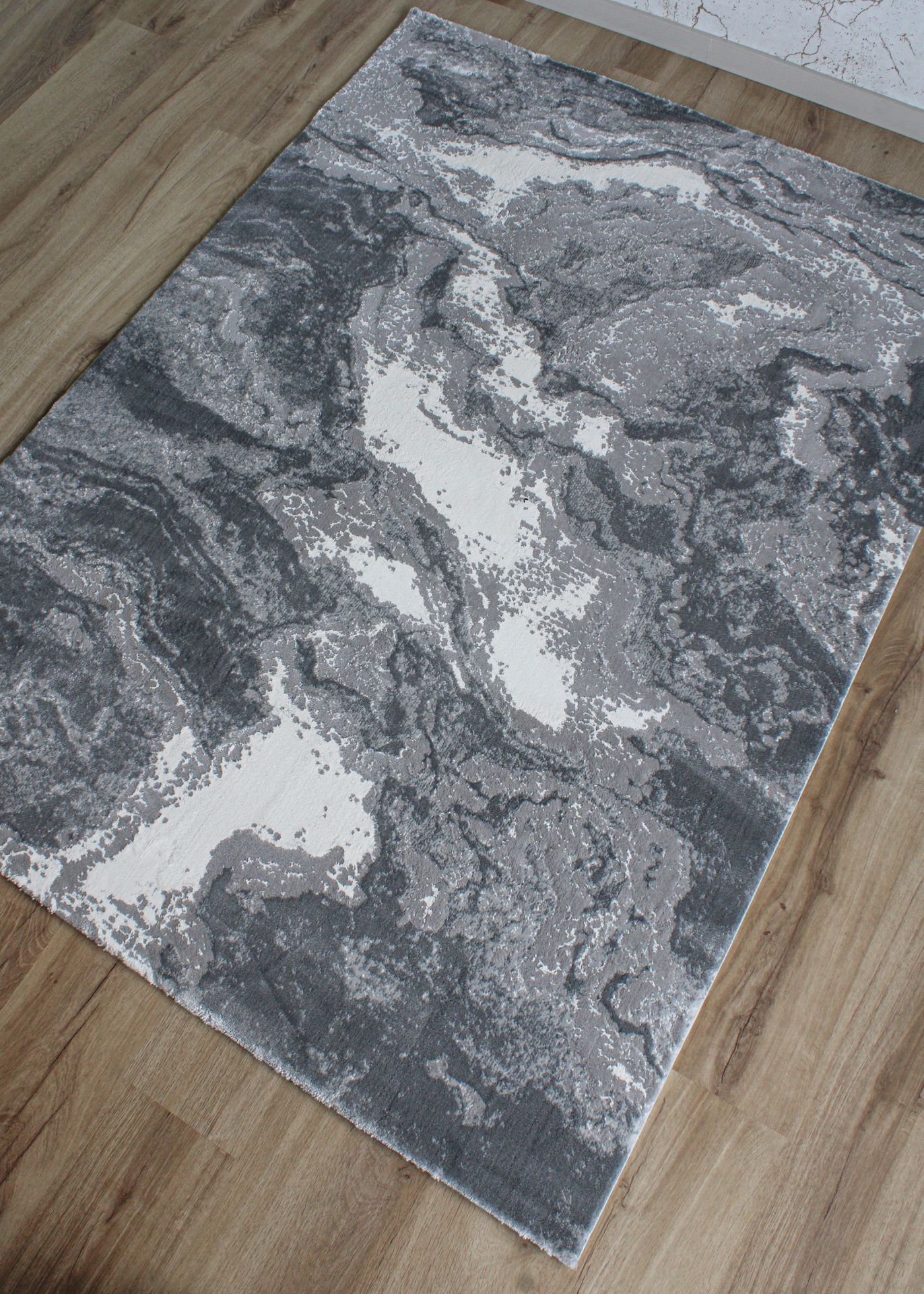 Tapete com padrão abstrato cinza e branco sobre chão de madeira clara