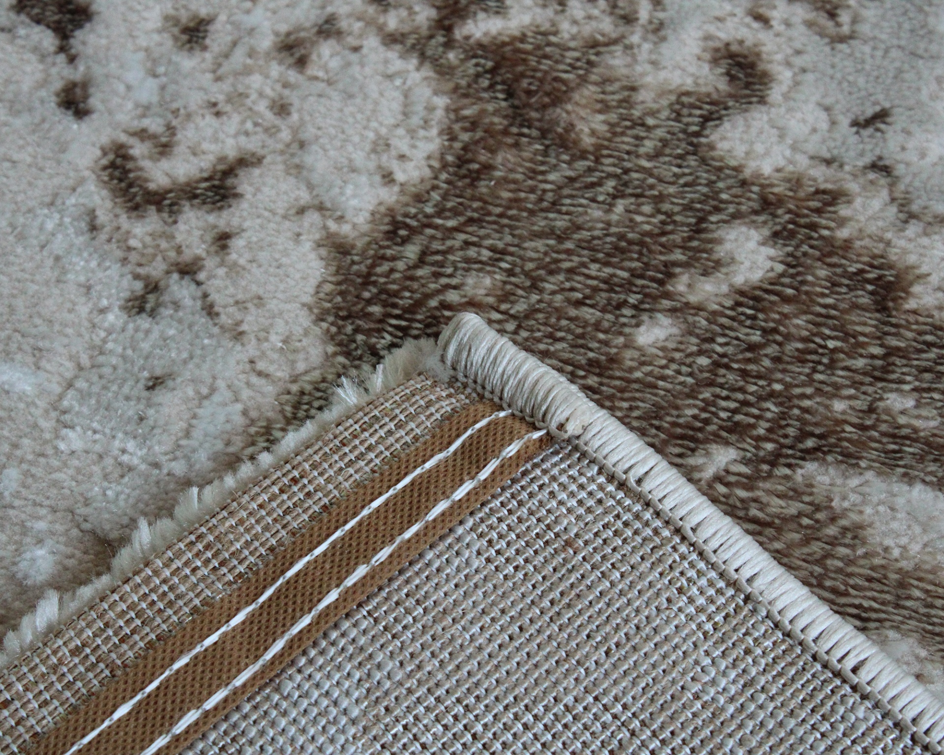 Tapete com padrão abstrato em tons de castanho e bege, borda costurada reforçada.