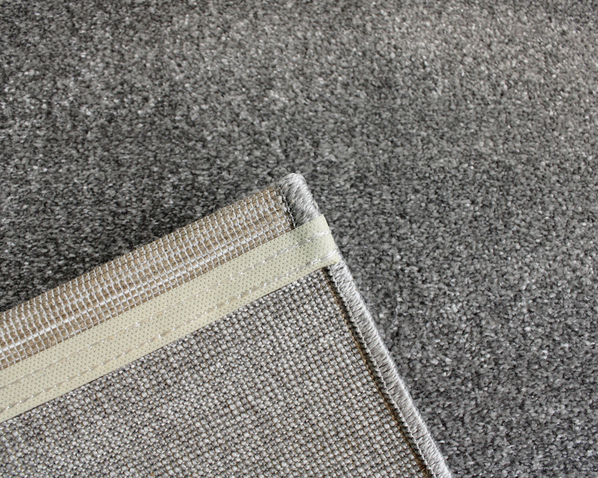 Canto de tapete cinza claro com bordas costuradas sobre carpete cinza.