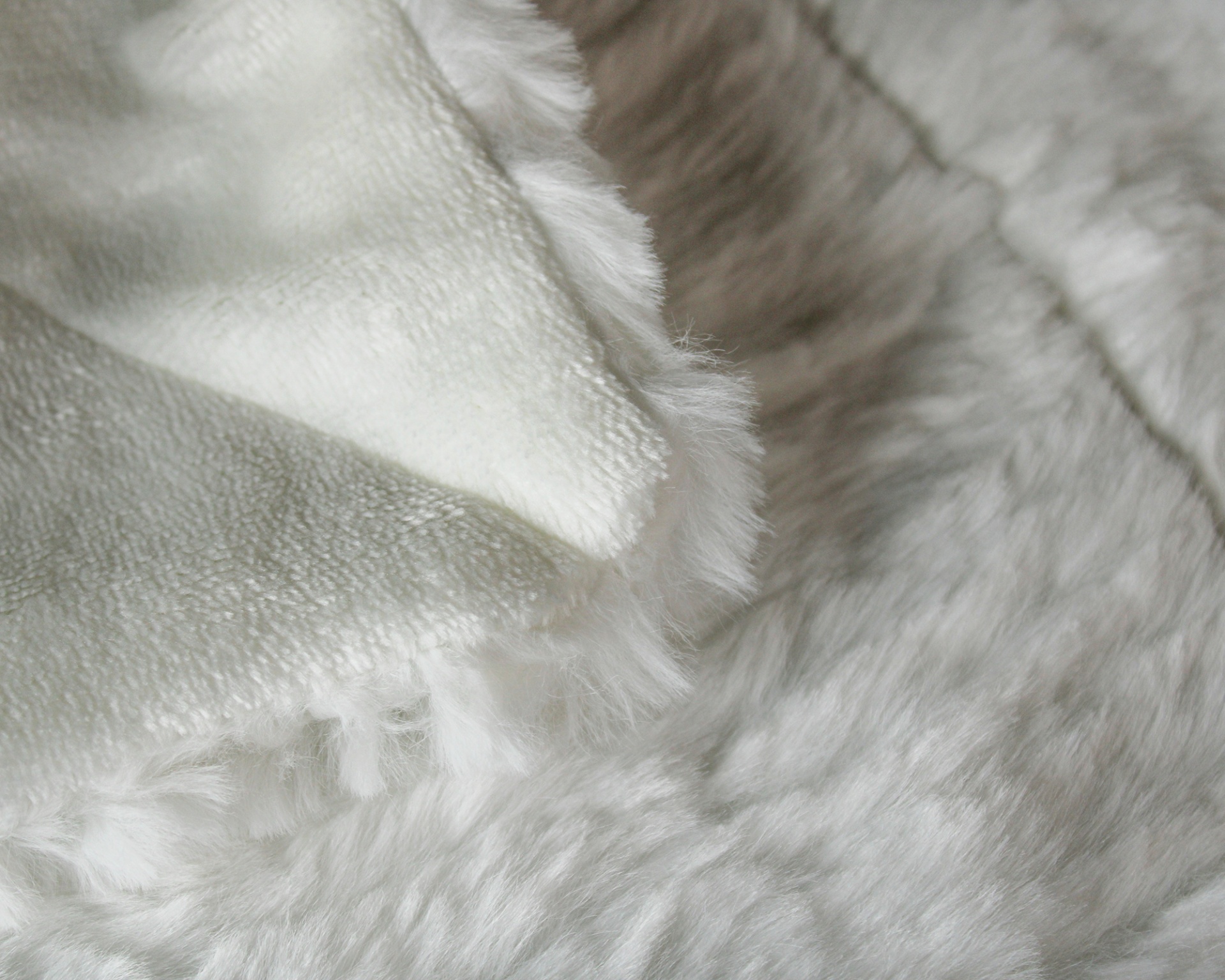 Manta felpuda branca com franjas sobre superfície cinza felpuda