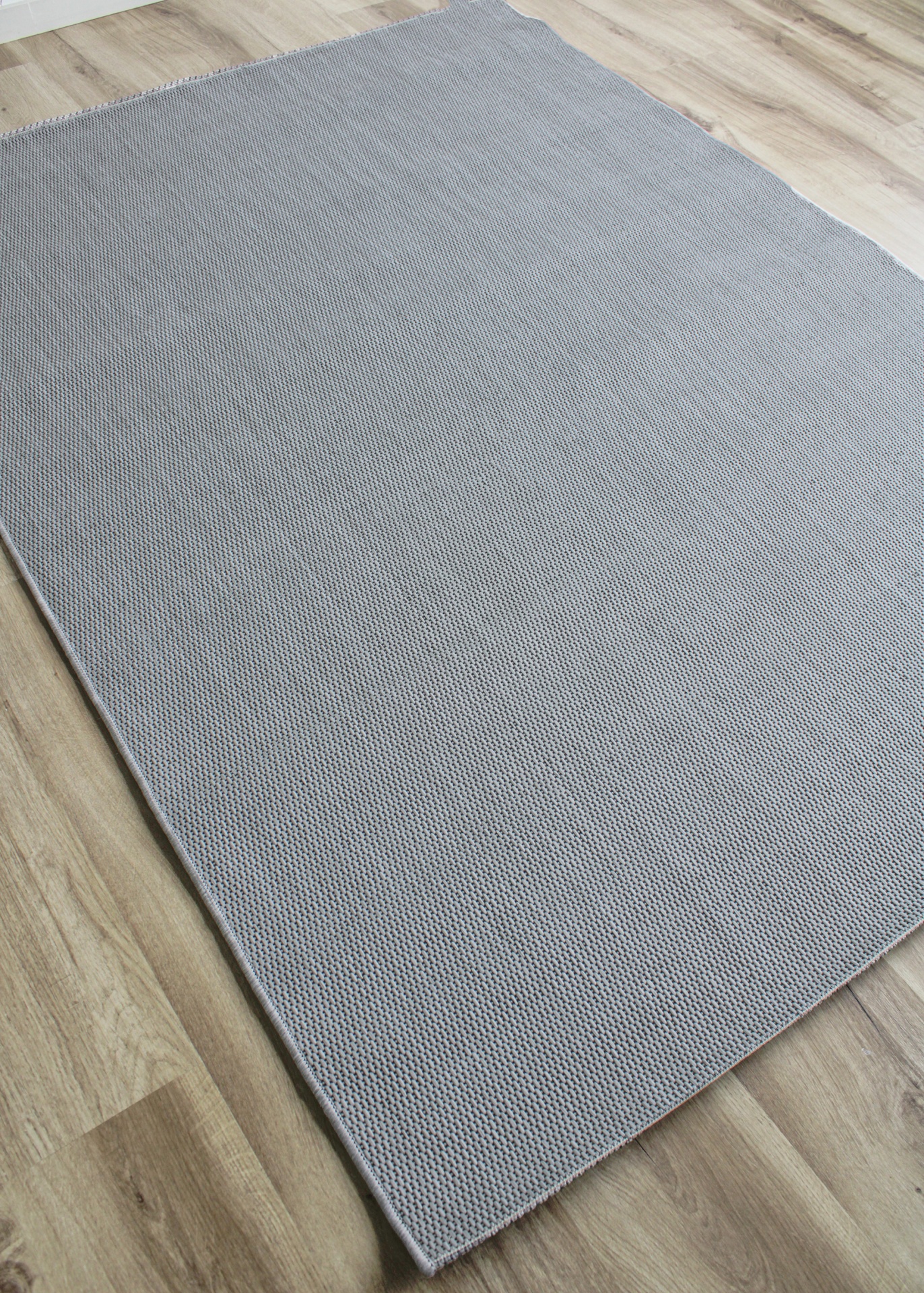 Tapete cinza claro com textura de malha sobre piso de madeira clara