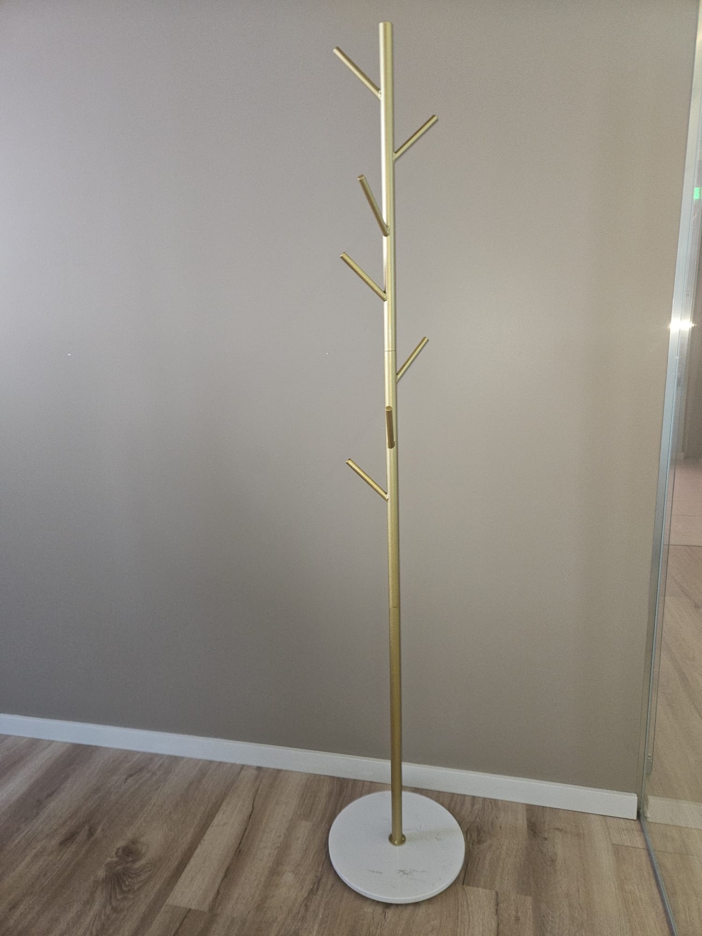 Cabideiro dourado com base branca de mármore num quarto de chão em madeira