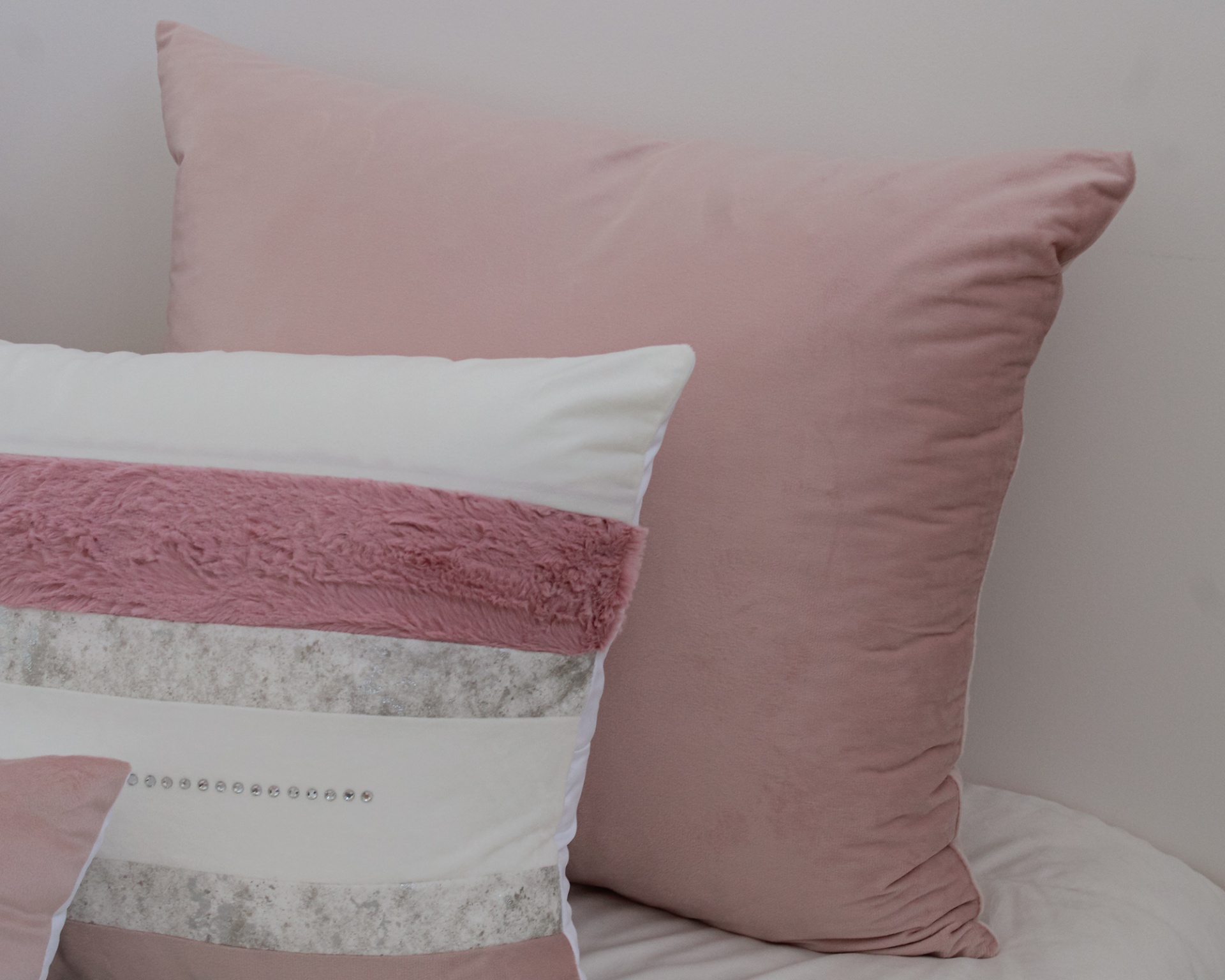 Almofadas decorativas em tons de rosa e cinza sobre cama clara