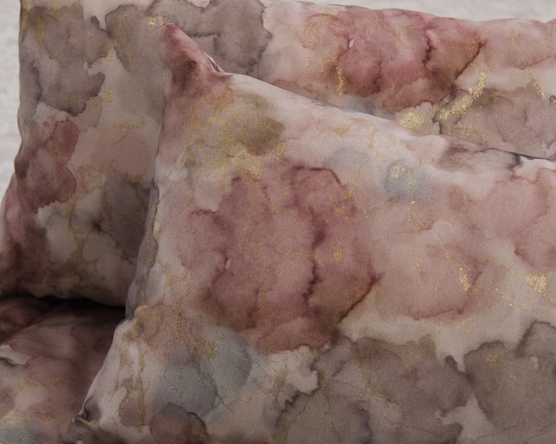 Almofadas decorativas com padrão em aquarela em tons rosa e cinza com detalhes dourados