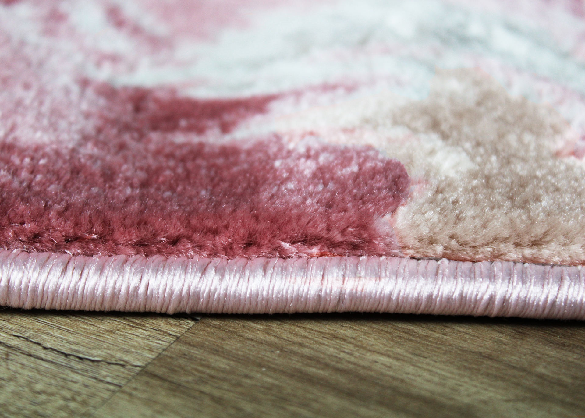 Borda de tapete felpudo em tons de rosa, vermelho e bege sobre chão de madeira clara