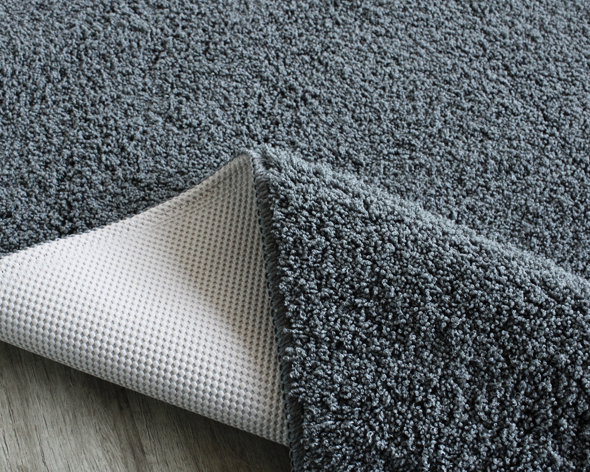 Tapete cinza felpudo com base antiderrapante branca em chão de madeira