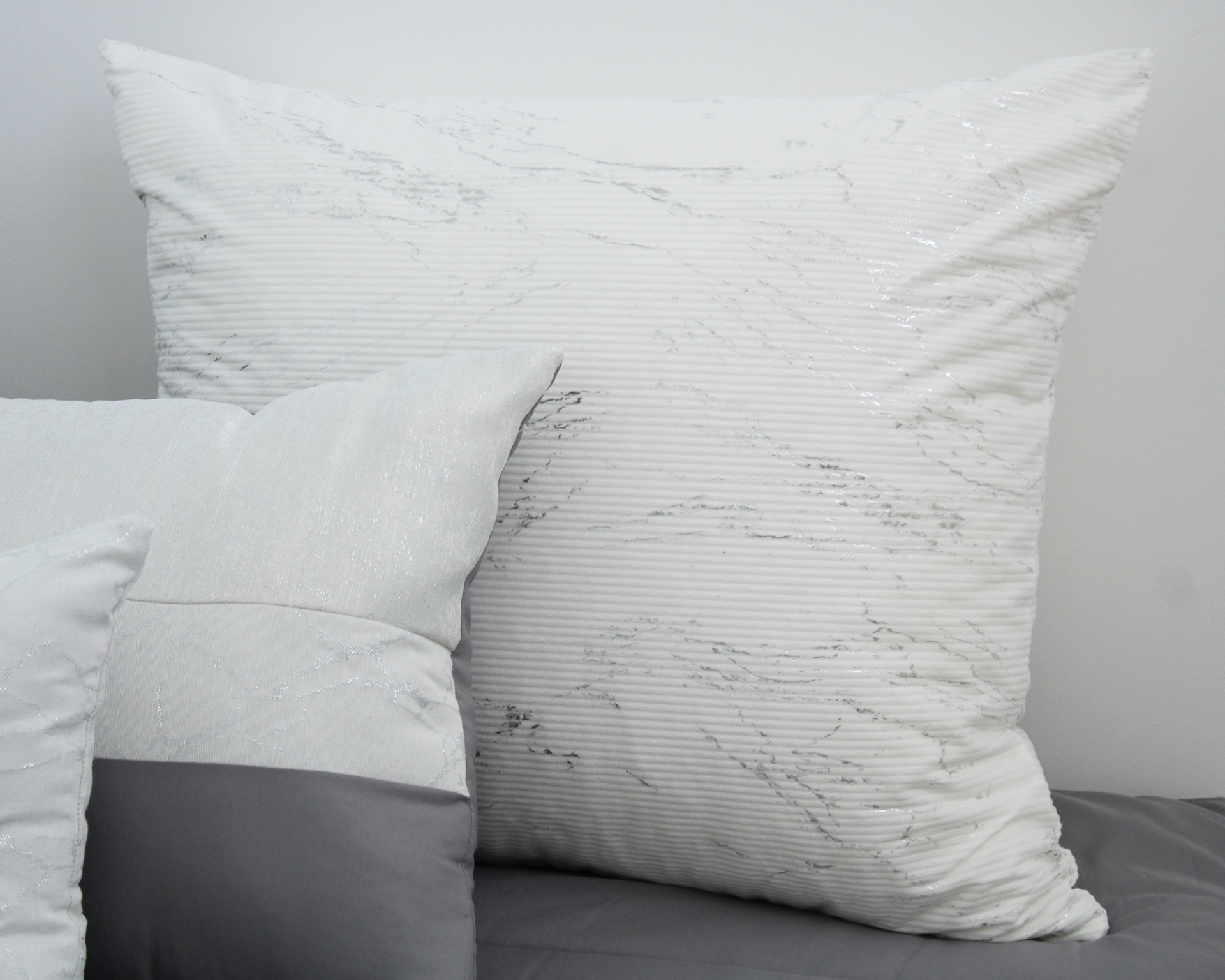 Três almofadas decorativas brancas e cinzentas sobre superfície cinzenta