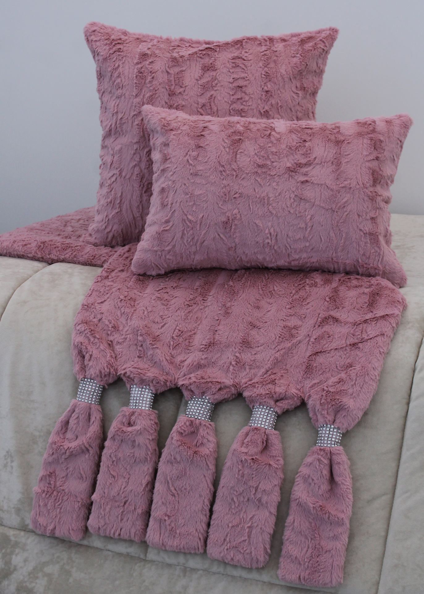 Almofadas e manta rosa felpudo com franjas prateadas sobre sofá cinzento