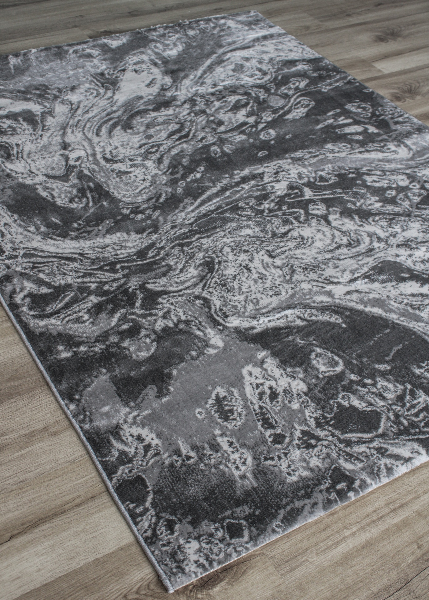 Tapete cinza e branco com padrão abstracto sobre chão de madeira