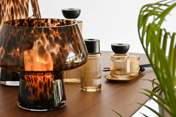 Frascos de vidro âmbar e bege com tampas pretas sobre mesa de madeira, com planta ao lado