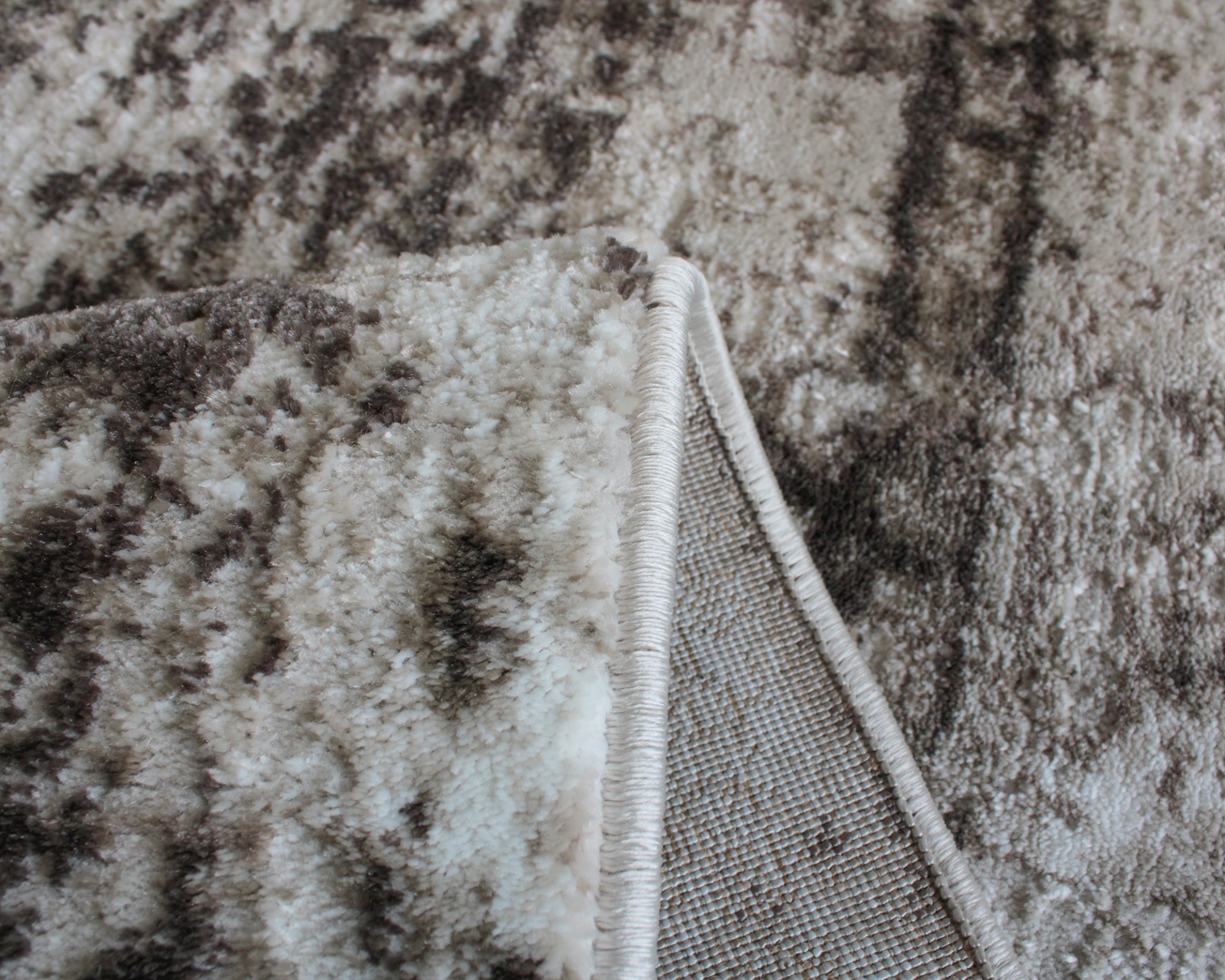 Tapete cinza e branco com padrão abstrato e textura felpuda dobrado mostrando o verso.