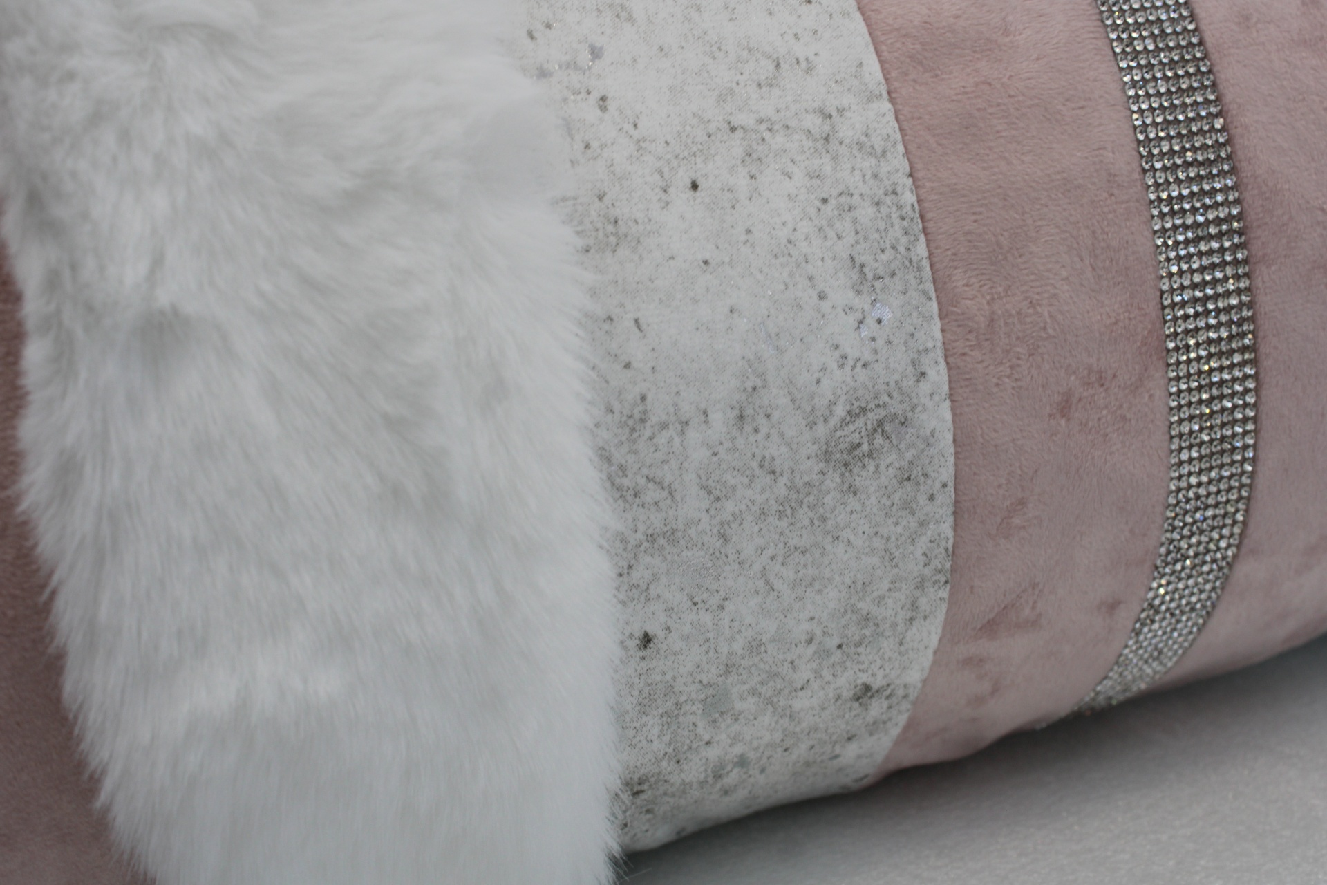 Faixas texturizadas branca felpuda, cinza manchada e rosa com pedraria numa almofada