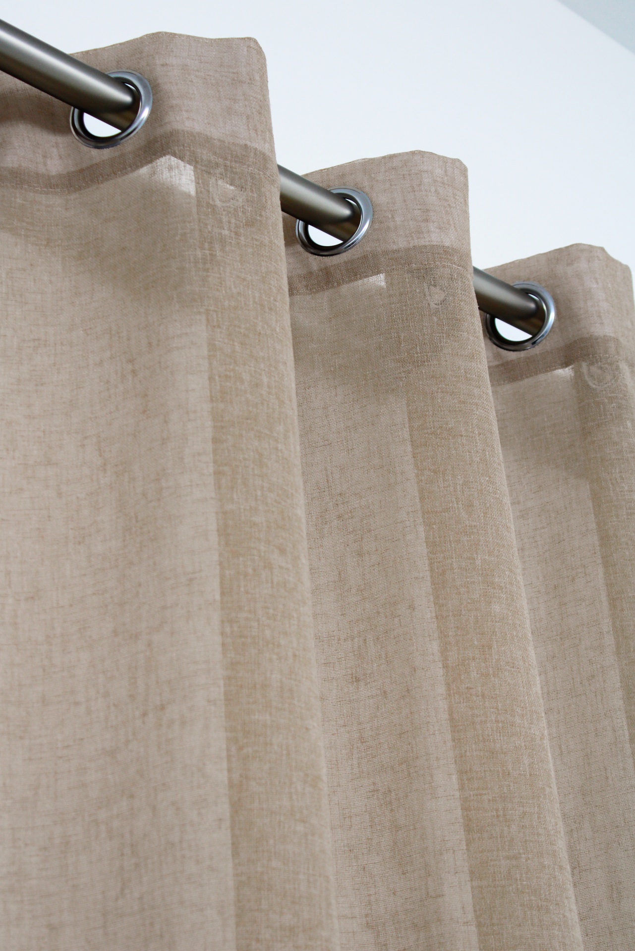 Cortina bege claro com ilhós metálicos pendurada numa barra prateada