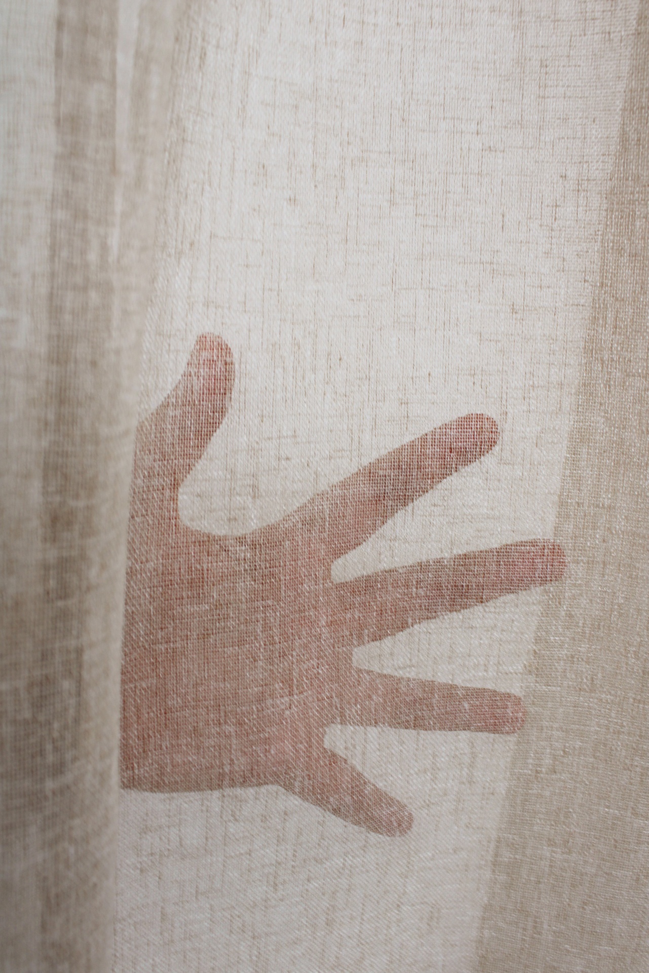 Cortina bege semi-transparente com textura e mão vista através do tecido