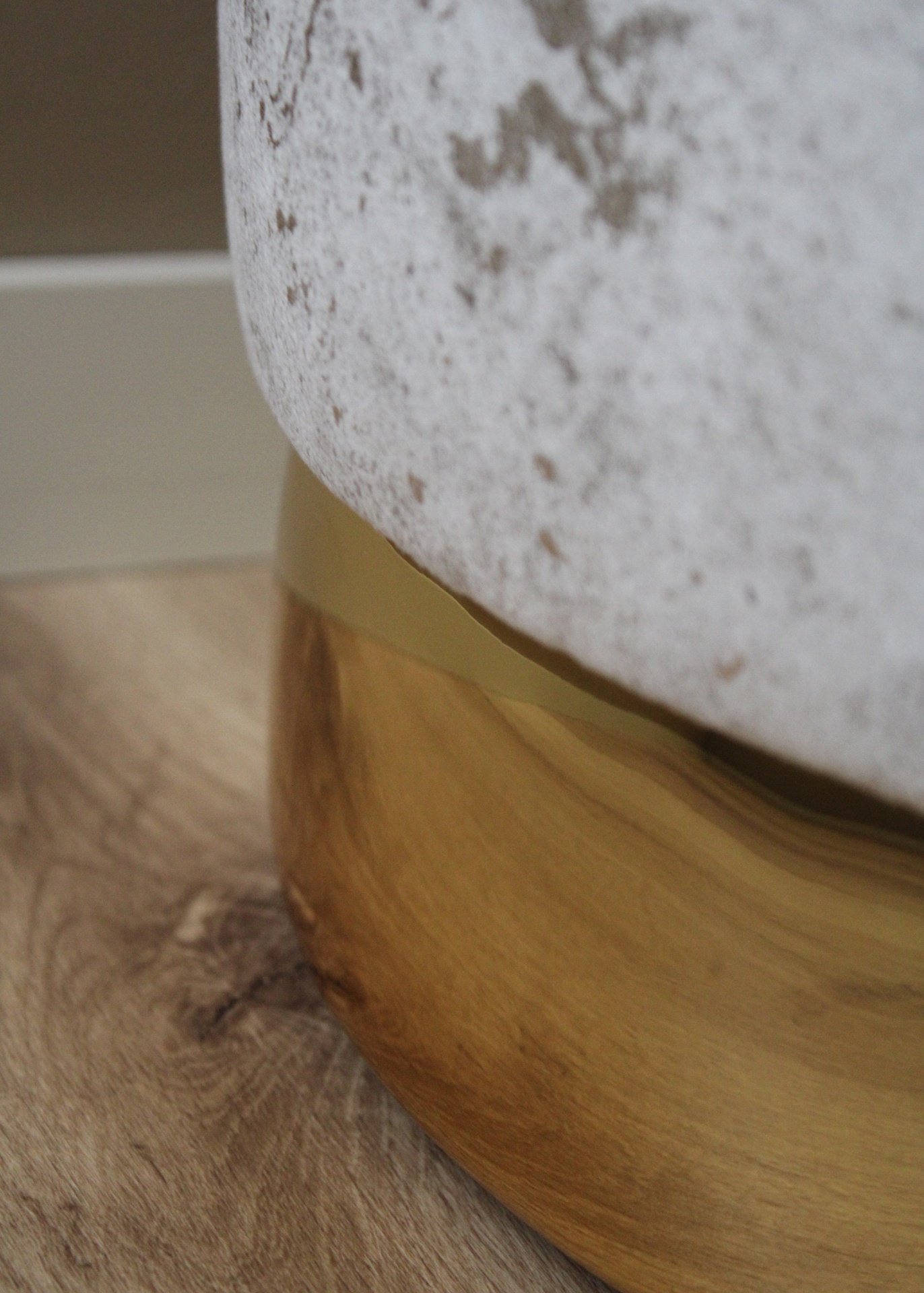 Pufe estofado branco com base dourada sobre chão de madeira