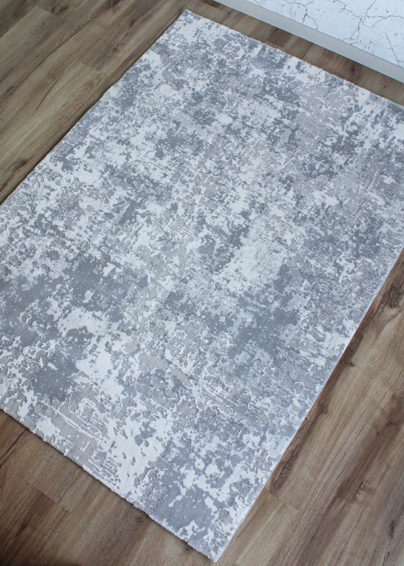 Tapete cinza e branco com padrão abstrato sobre chão de madeira