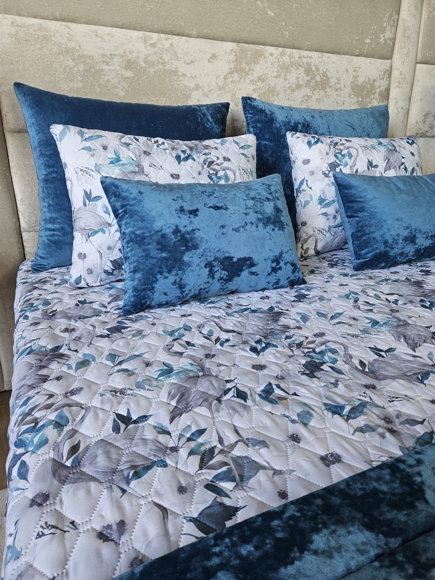 Almofadas azul veludo e branco floral com edredão combinado numa cama