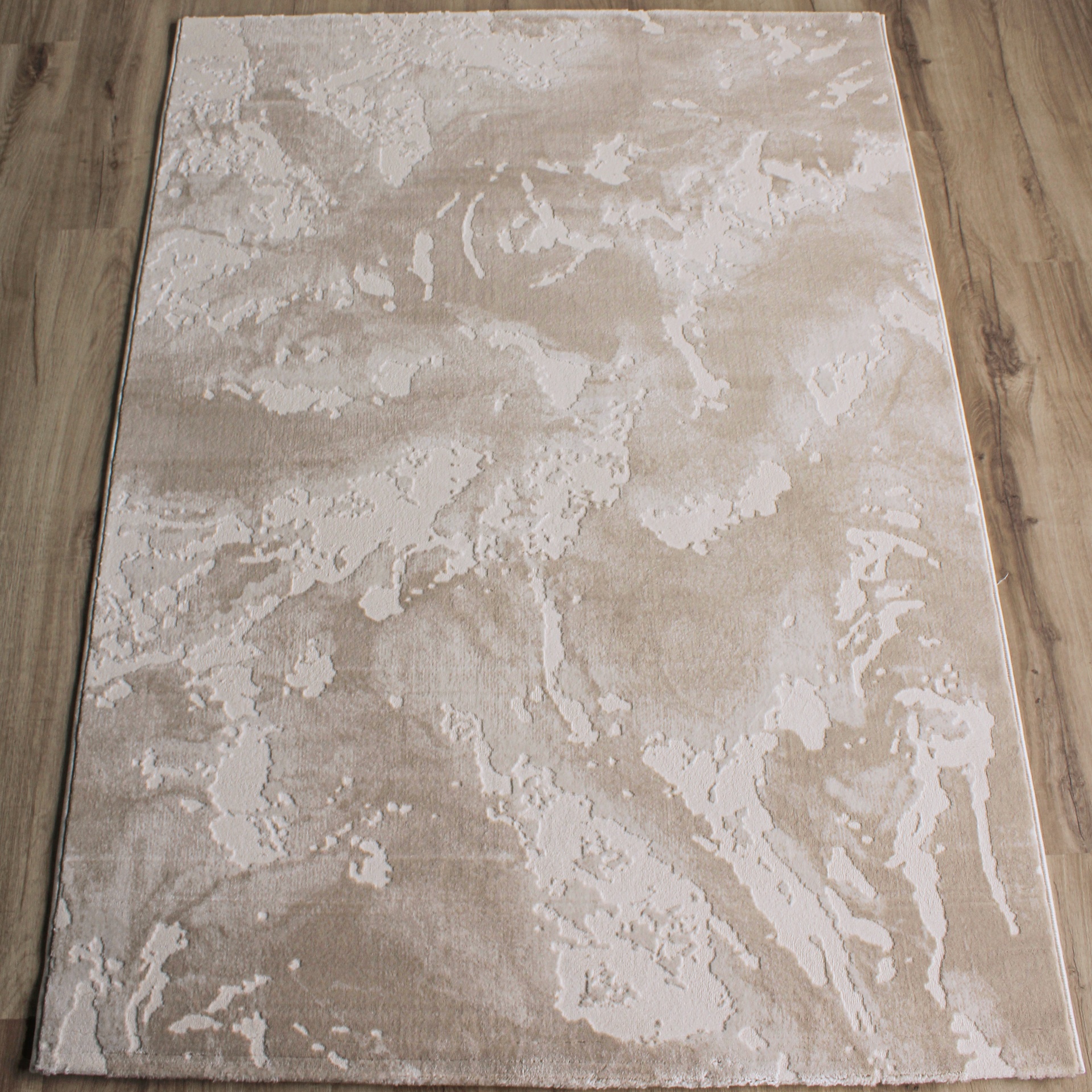 Tapete retangular bege com padrão abstrato sobre chão de madeira clara