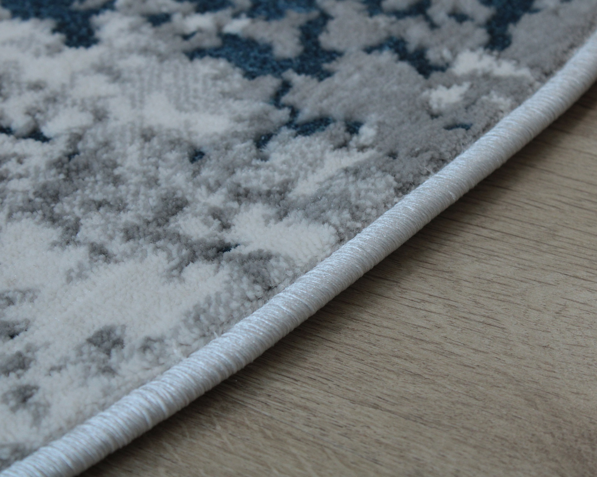 Tapete cinzento e branco com padrão abstrato e borda azul clara no chão de madeira