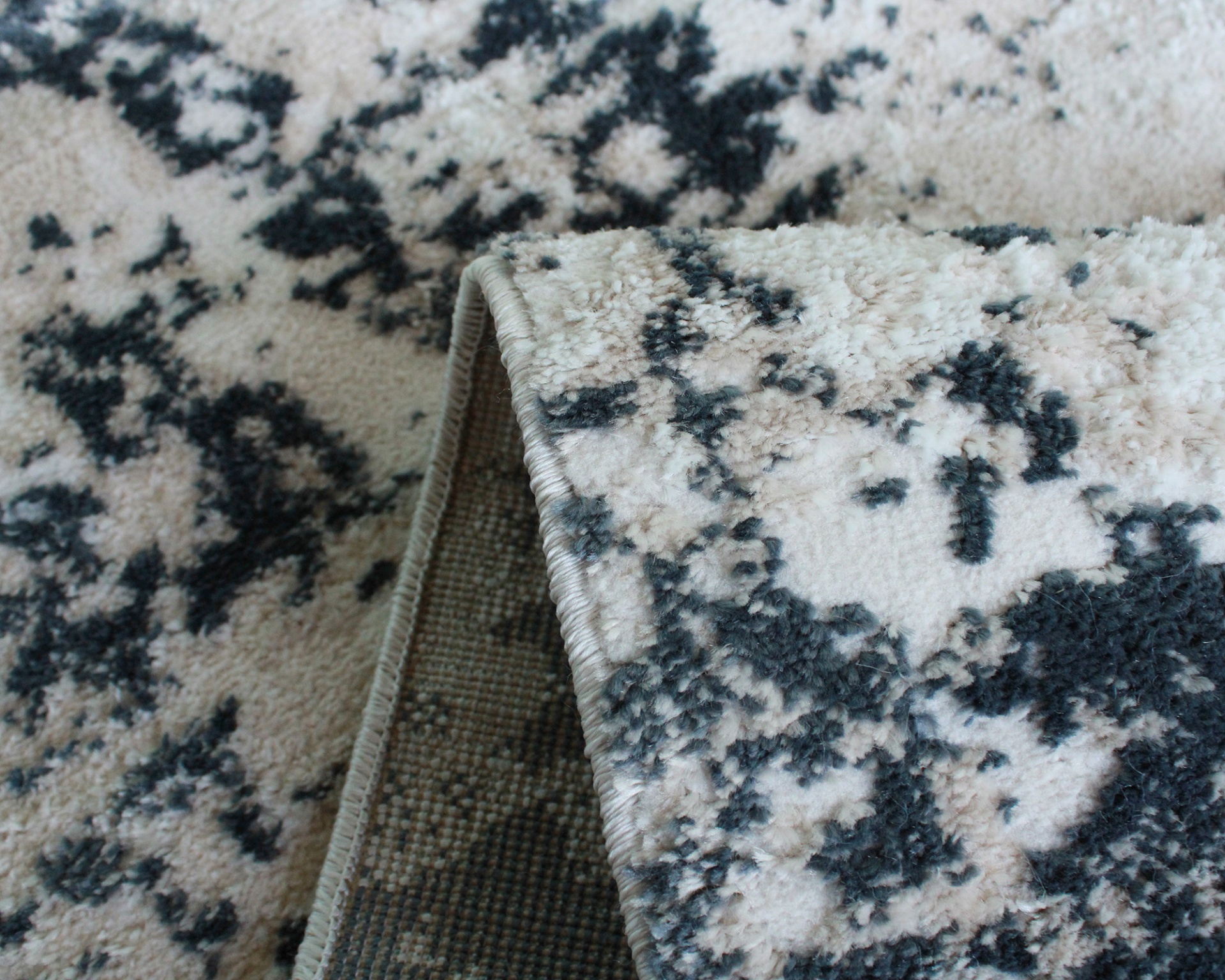 Tapete felpudo padrão abstracto bege e preto com dobra mostrando verso