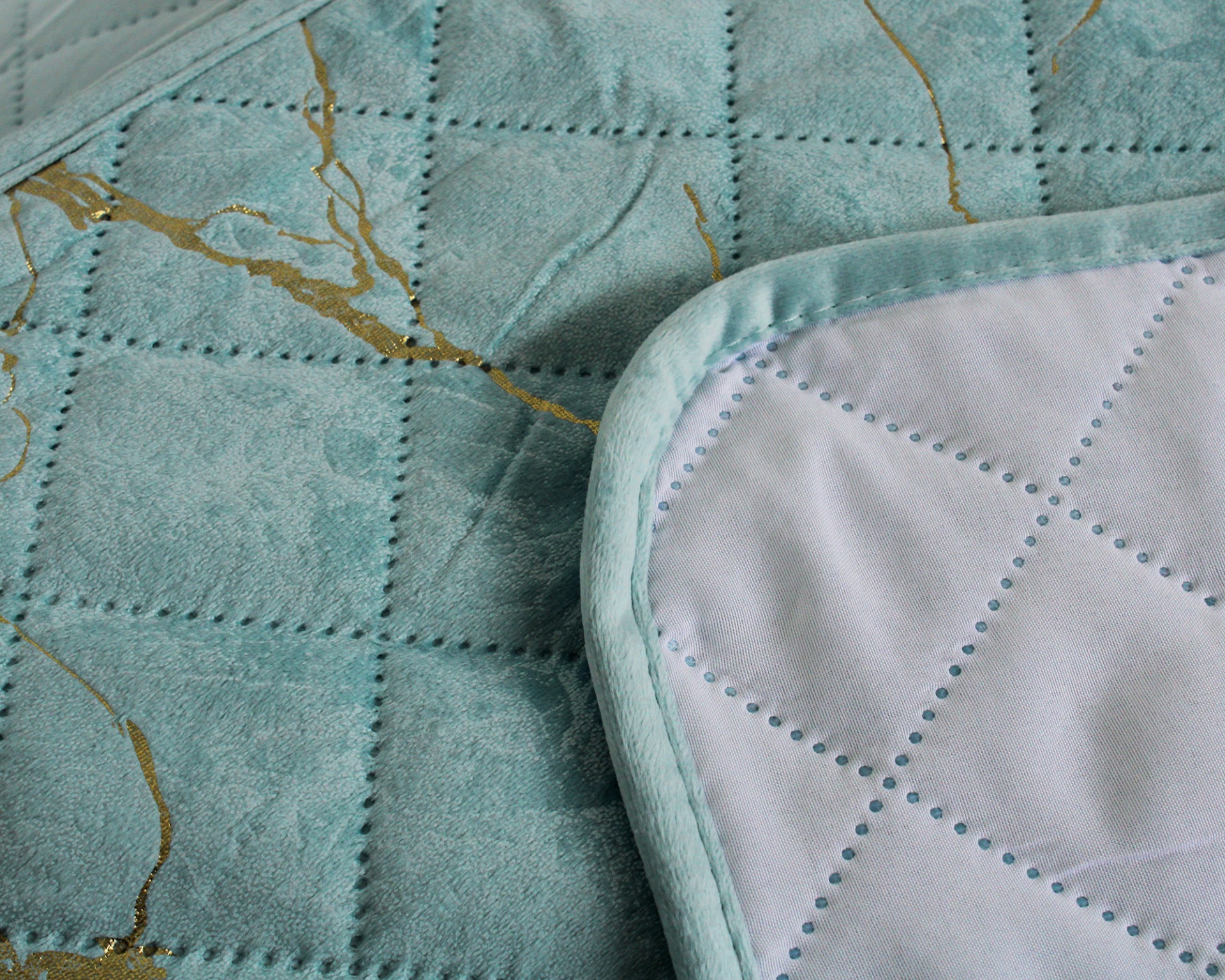 Colcha azul clara acolchoada com detalhes dourados e remate bordado