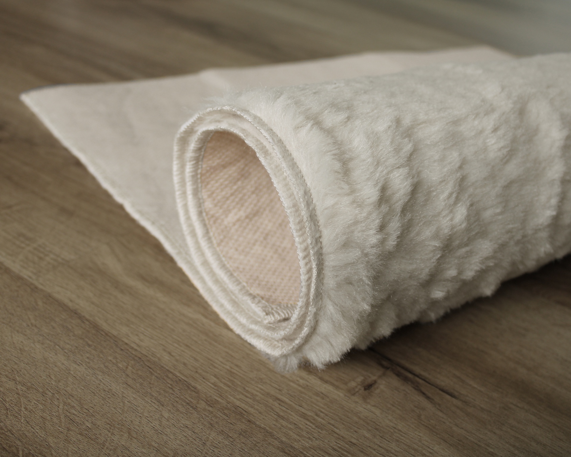 Tapete branco felpudo parcialmente enrolado sobre chão de madeira