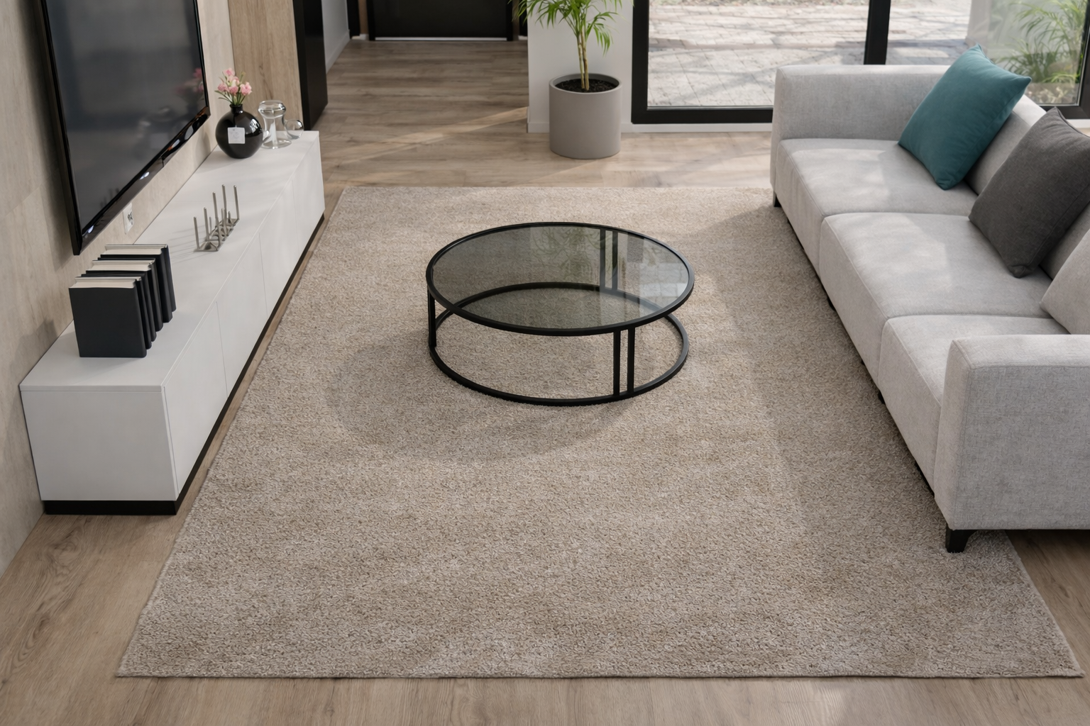 Tapete bege de pelo alto numa sala com mesa de centro de vidro e metal preto, sofá cinza com almofadas coloridas, móvel branco e TV de parede.