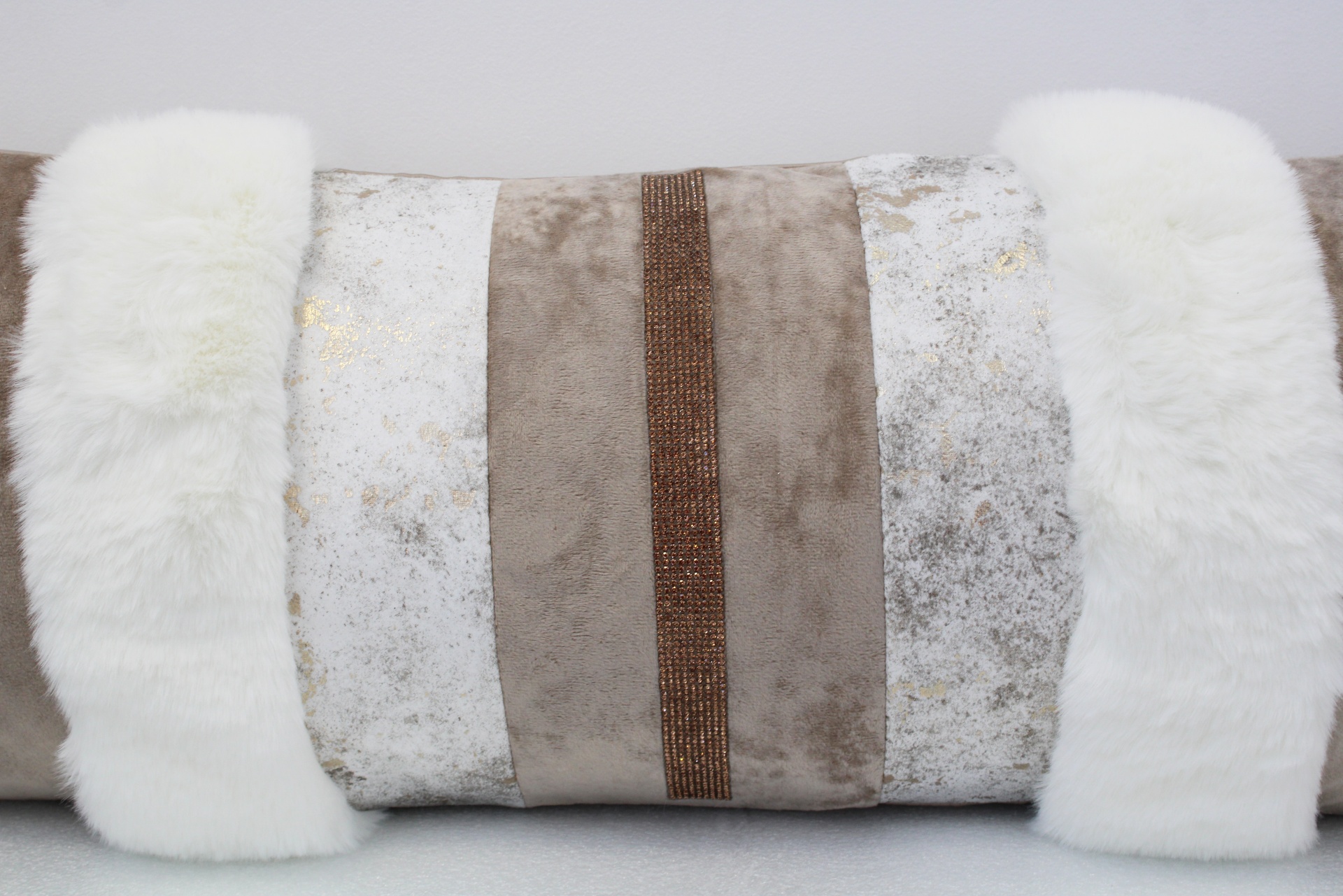 Almofada retangular com pele sintética branca e tecidos bege e branco com padrão abstrato.