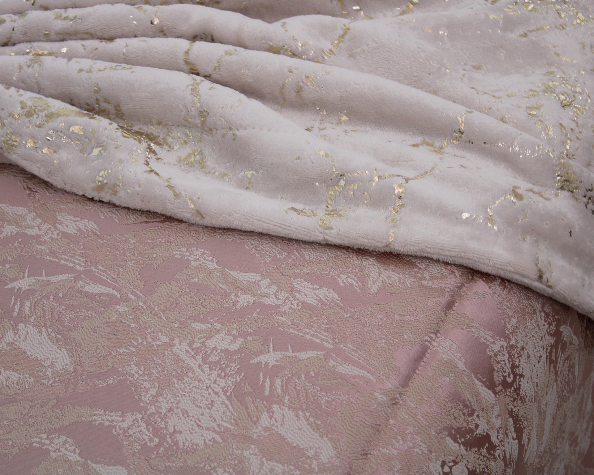 Manta creme com detalhes dourados sobre colcha rosa texturizada