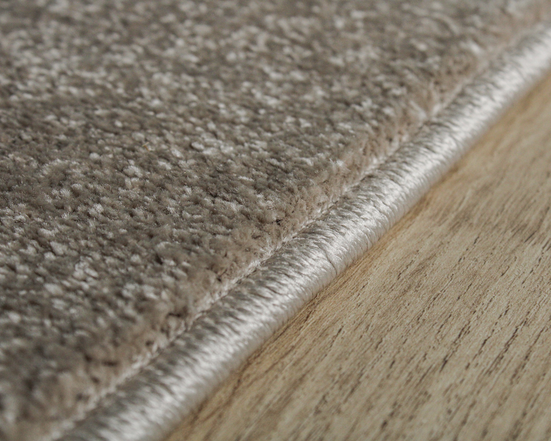 Tapete bege com textura macia e borda prateada sobre pavimento de madeira clara