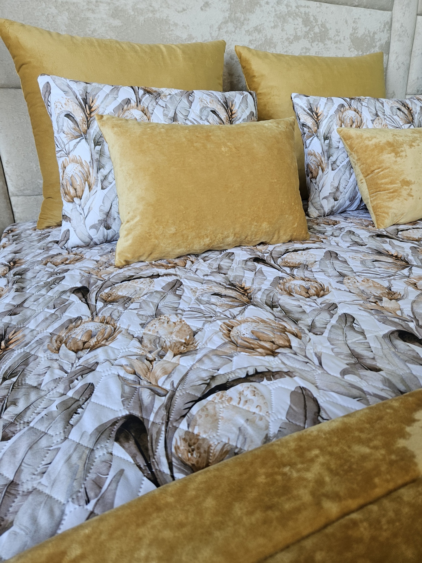 Conjunto de almofadas e colcha floral com almofadas mostarda em veludo numa cama.