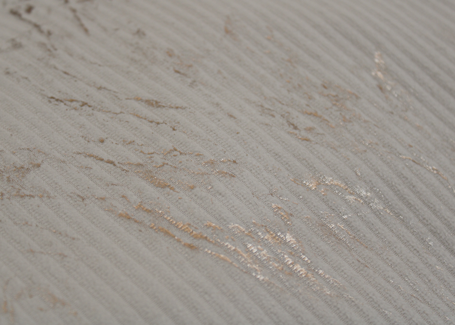 Superfície texturada bege claro com riscas finas e manchas douradas.