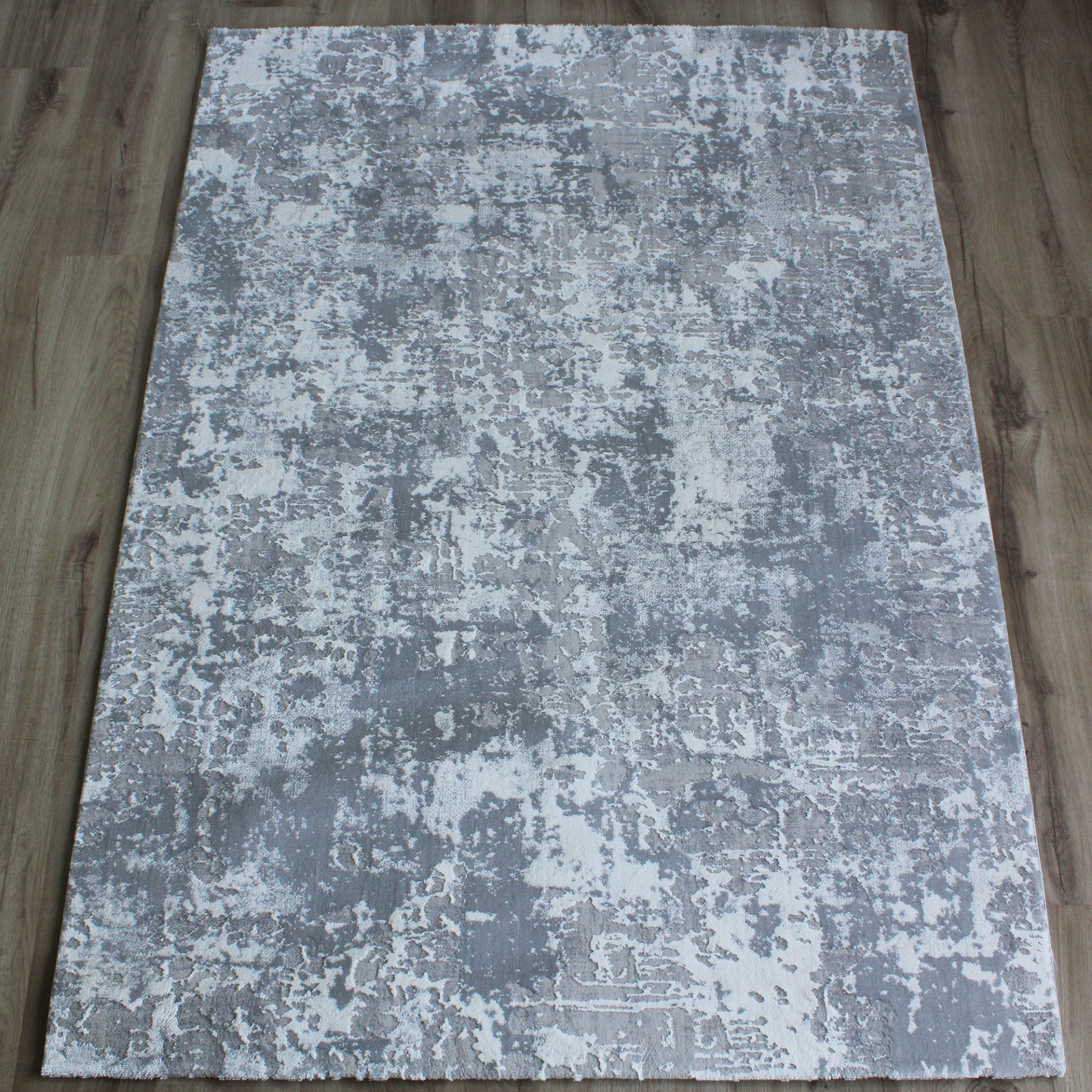 Tapete cinzento claro e branco com padrão abstrato sobre chão de madeira.