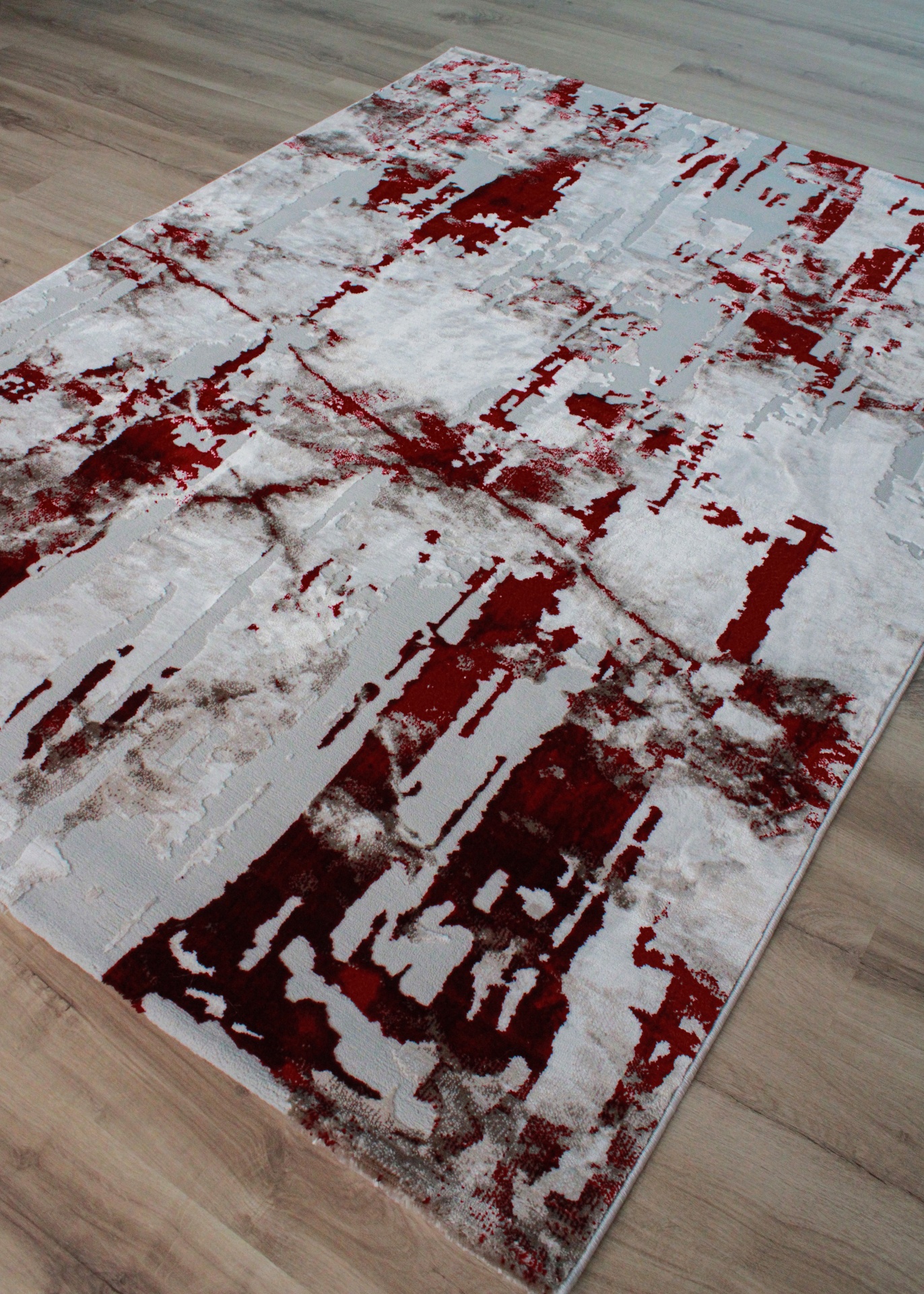 Tapete retangular com padrão abstrato vermelho, branco e cinzento sobre chão de madeira clara