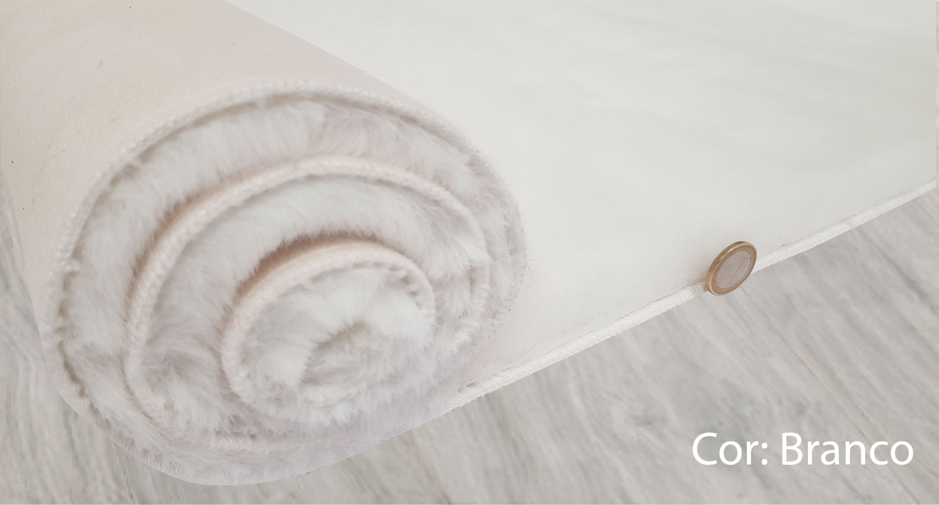 Rolo de tecido branco macio parcialmente desenrolado no chão cinza claro com moeda para escala.